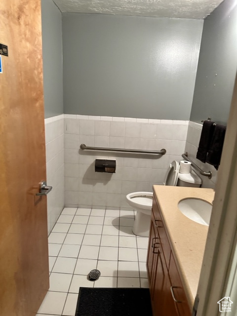 Bathroom with tile flooring, vanity, toilet, and tile walls