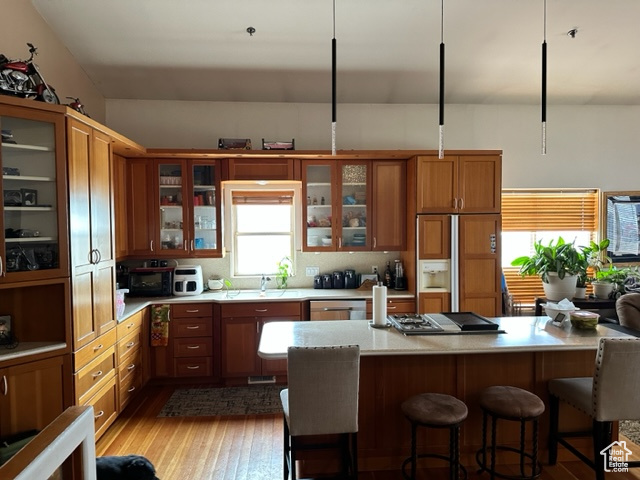 Kitchen with wood-type flooring, hanging light fixtures, a breakfast bar, appliances with stainless steel finishes, and sink
