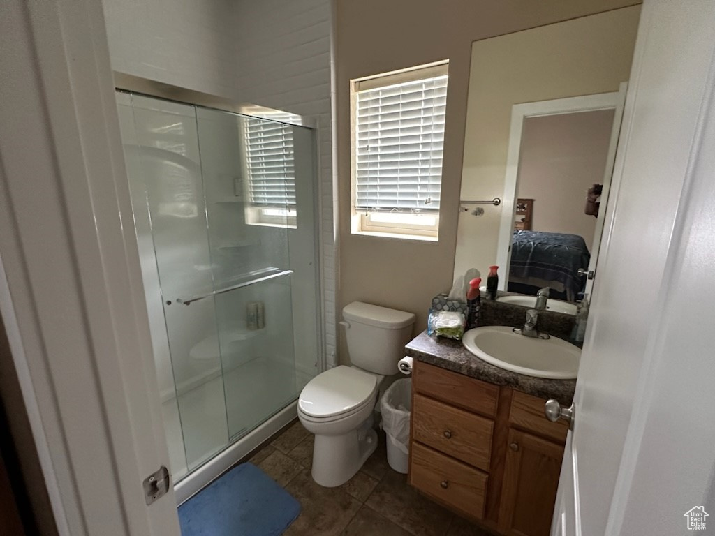 Bathroom with a shower with shower door, toilet, tile flooring, and large vanity