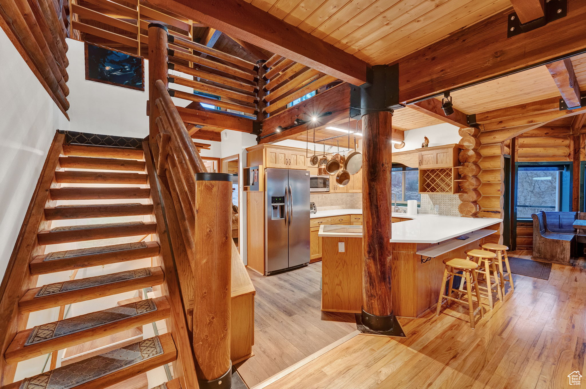 Kitchen with kitchen peninsula, appliances with stainless steel finishes, light hardwood / wood-style floors, beamed ceiling, and log walls