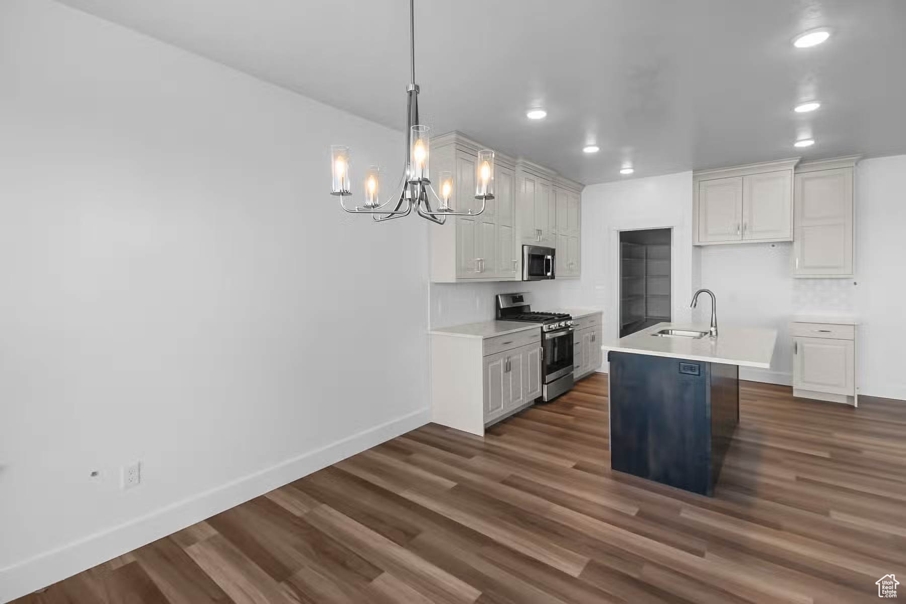 Kitchen with appliances with stainless steel finishes, pendant lighting, dark wood-type flooring, and a kitchen island with sink