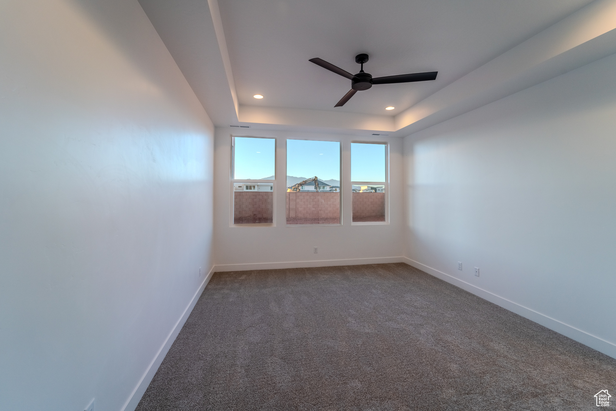 Carpeted spare room with ceiling fan and a raised ceiling