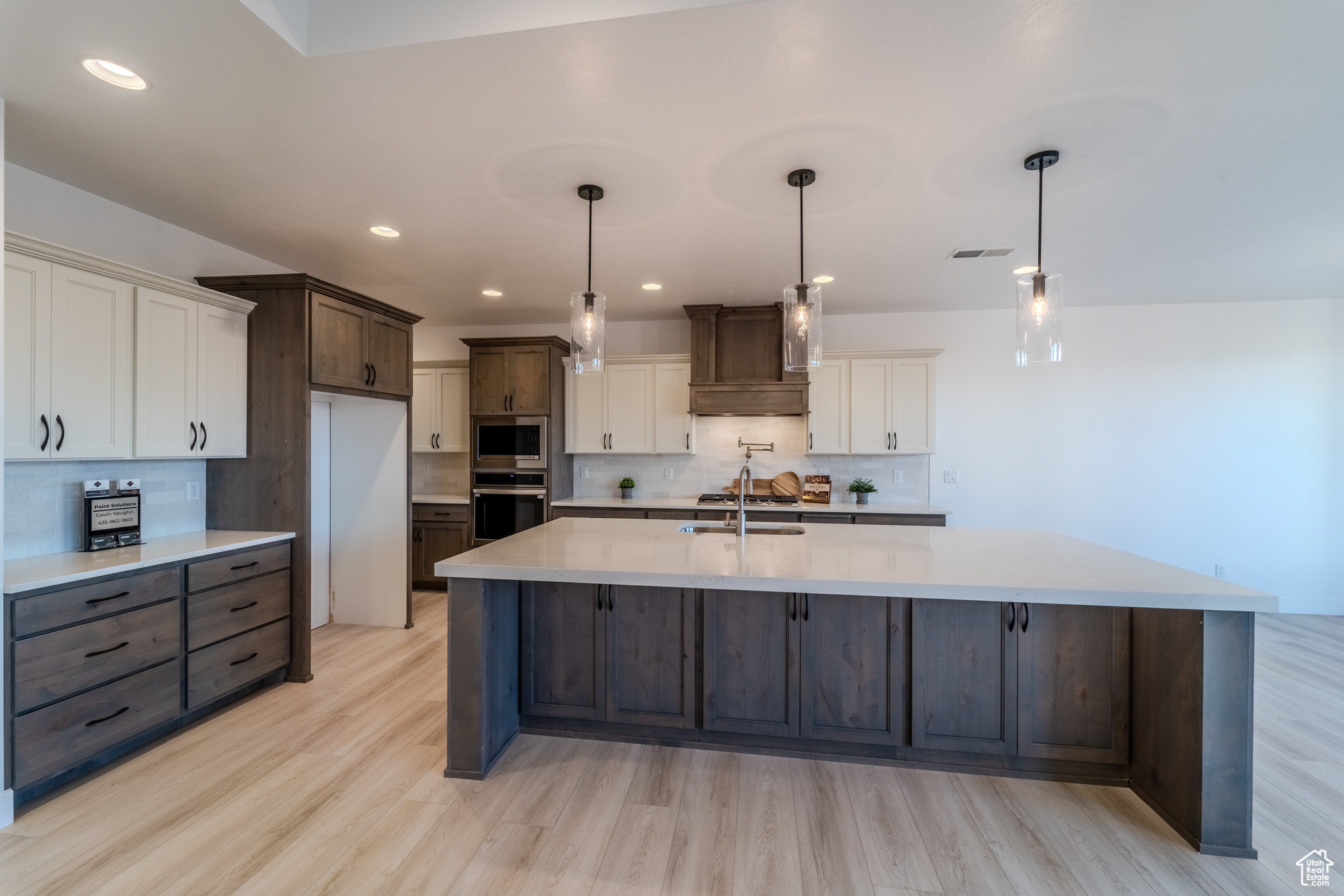 Kitchen featuring stainless steel appliances, light hardwood / wood-style floors, decorative backsplash, pendant lighting, and white cabinets