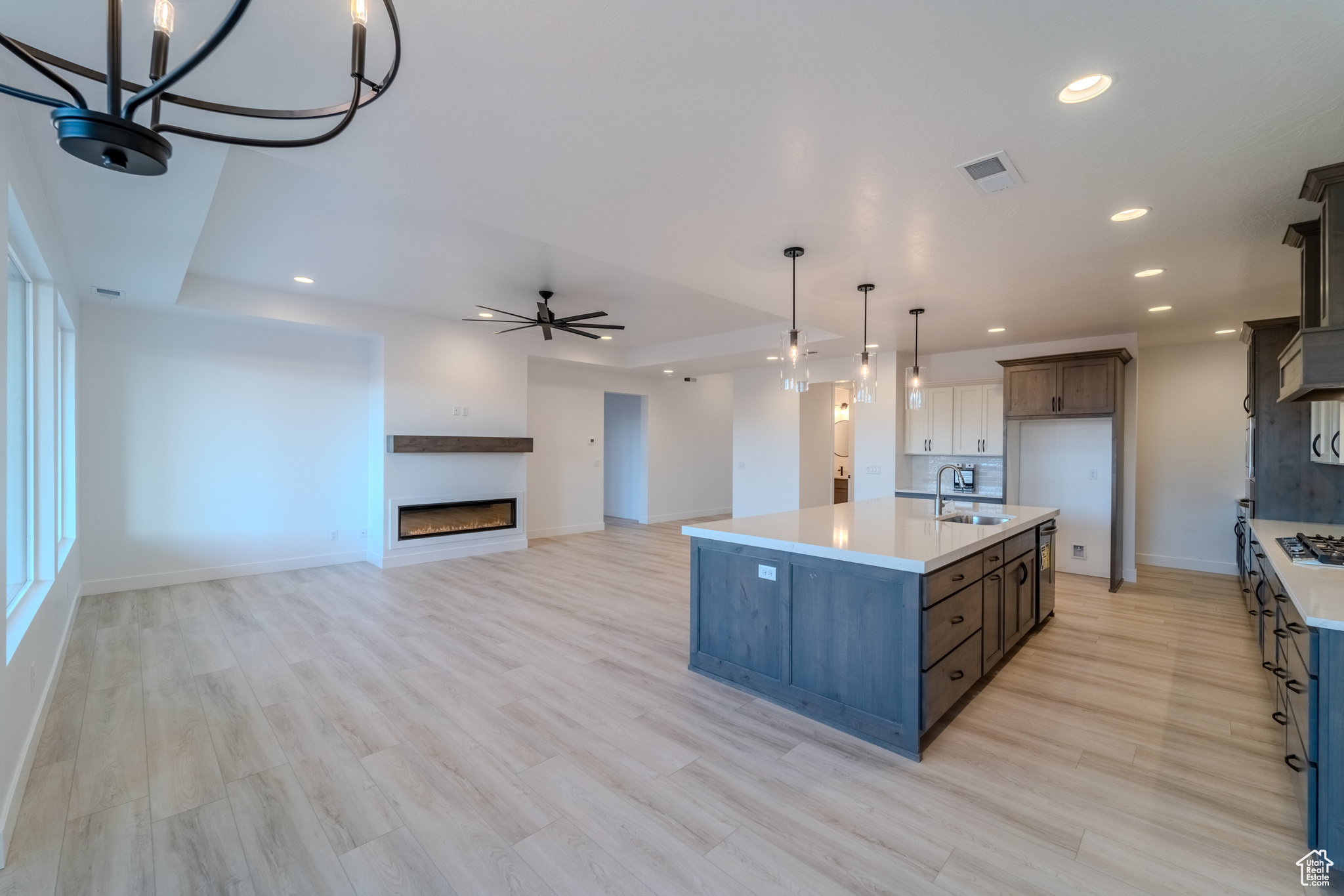 Kitchen featuring sink, decorative light fixtures, light hardwood / wood-style flooring, a kitchen island with sink, and ceiling fan with notable chandelier