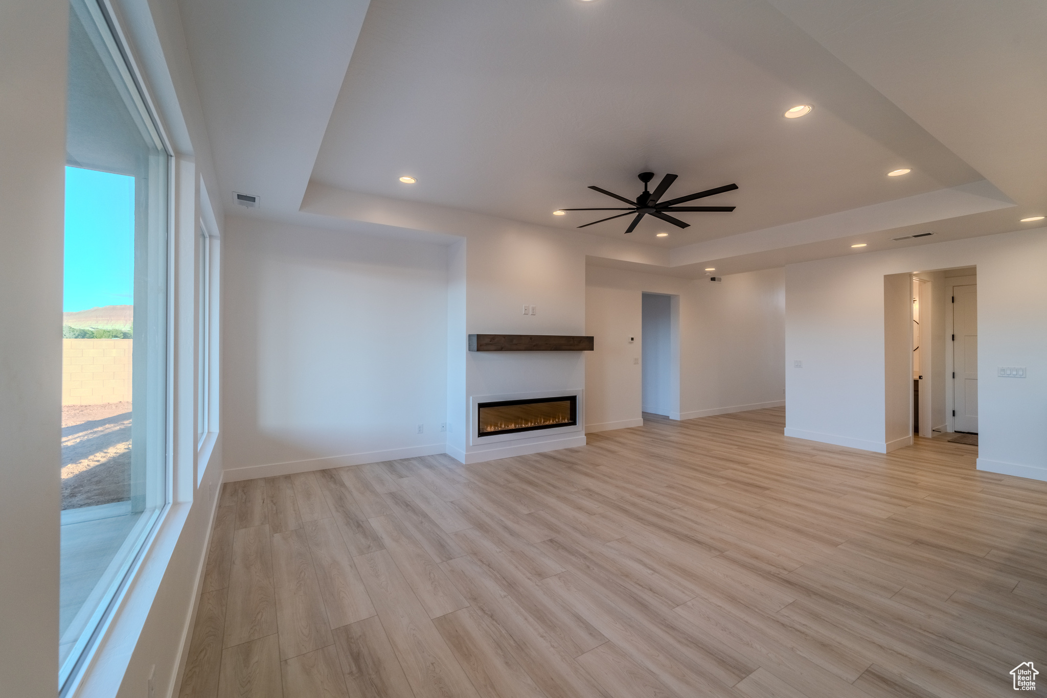 Unfurnished living room featuring ceiling fan, a raised ceiling, and light hardwood / wood-style flooring