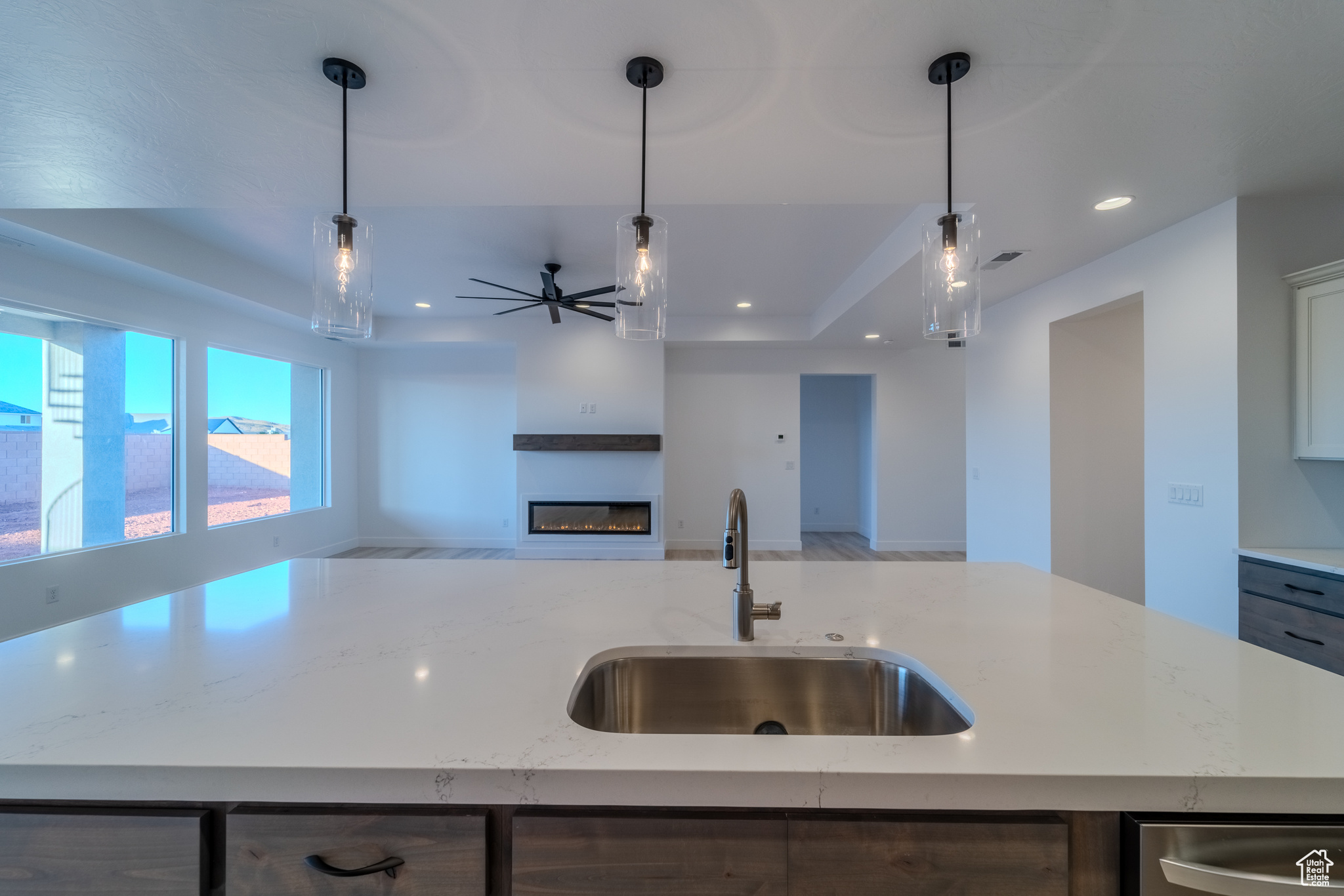 Kitchen with sink, decorative light fixtures, light stone counters, and an island with sink