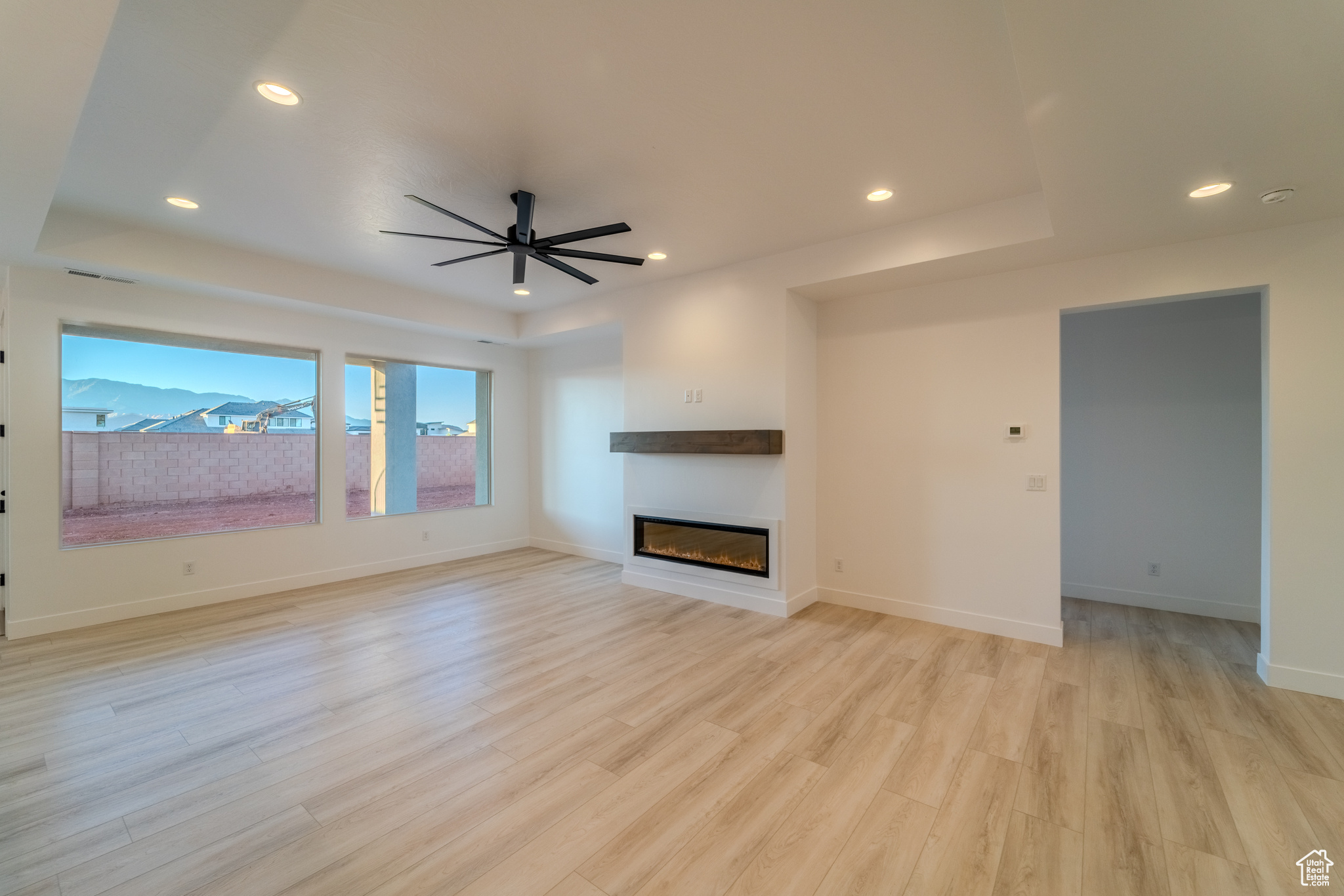 Unfurnished living room with ceiling fan, light hardwood / wood-style floors, and a tray ceiling