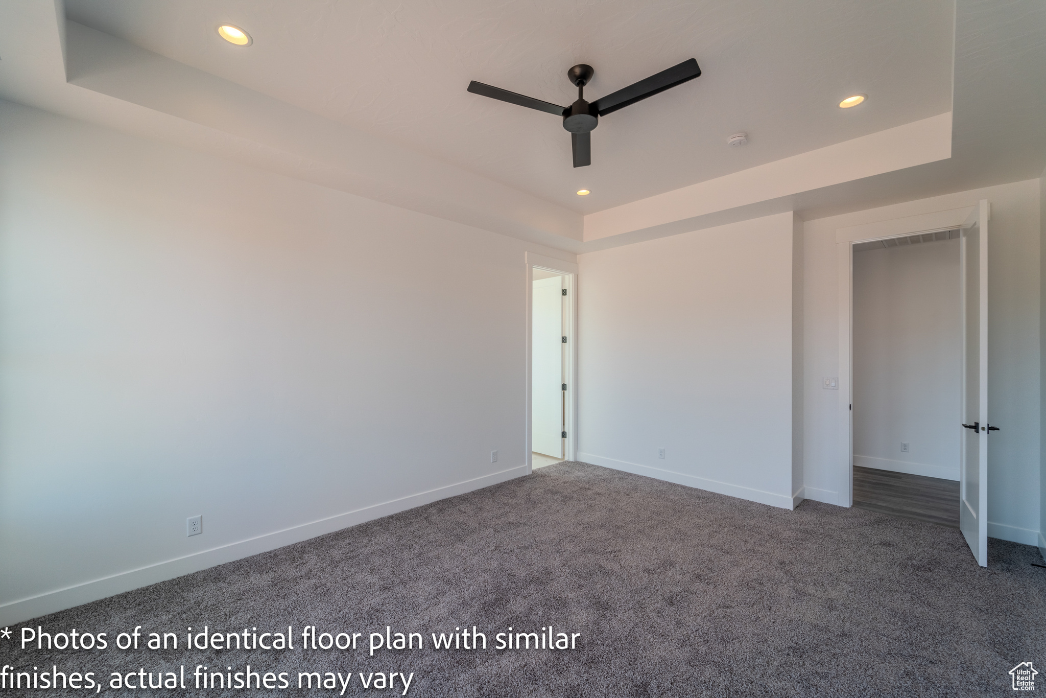 Carpeted empty room with ceiling fan and a tray ceiling