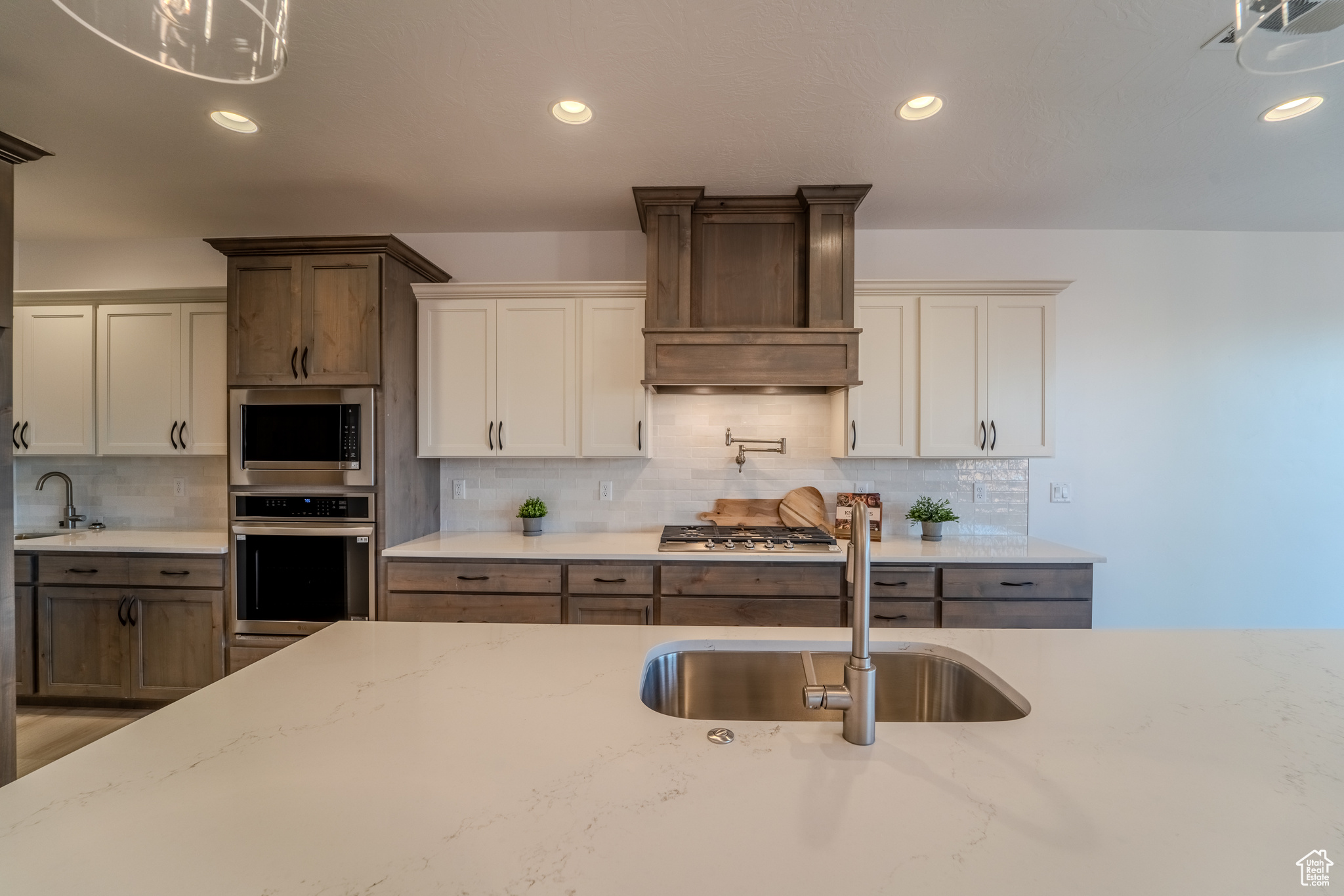 Kitchen with backsplash, custom exhaust hood, white cabinets, appliances with stainless steel finishes, and sink