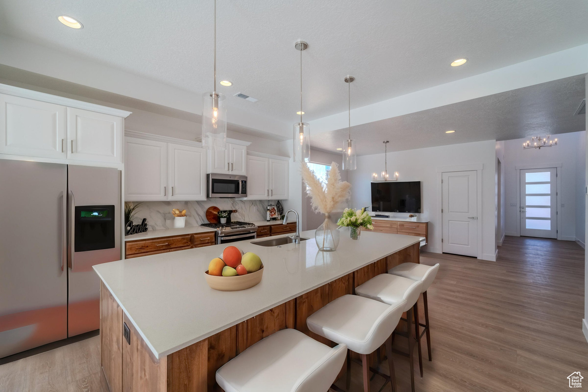 Kitchen with white cabinets, light hardwood / wood-style floors, appliances with stainless steel finishes, decorative backsplash, and a spacious island