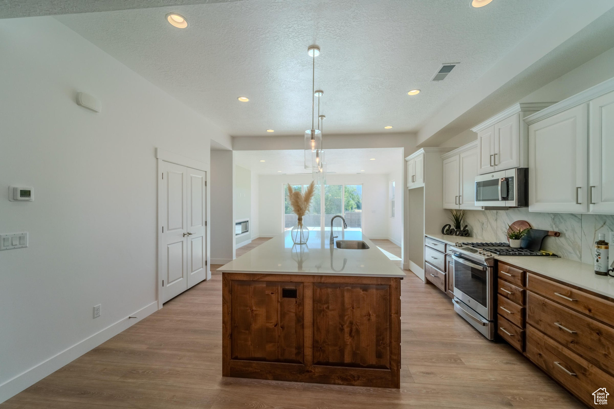 Kitchen with white cabinetry, stainless steel appliances, sink, light hardwood / wood-style flooring, and a kitchen island with sink