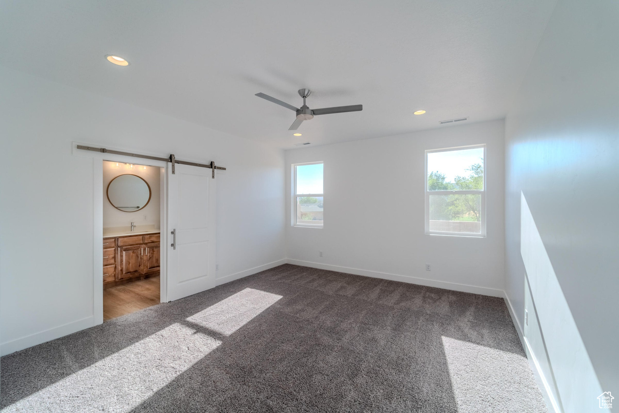 Unfurnished bedroom featuring carpet floors, ensuite bath, ceiling fan, and a barn door