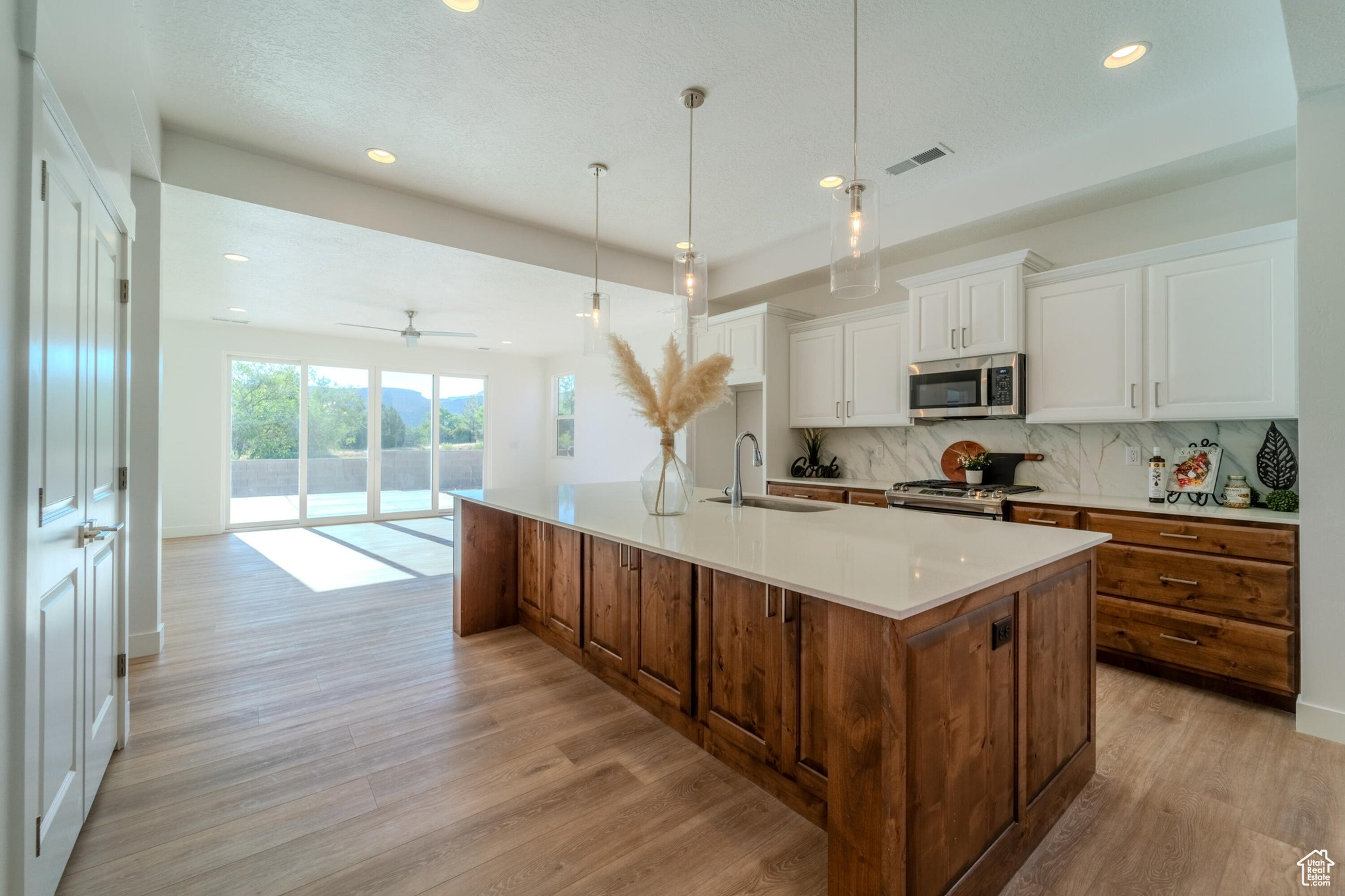 Kitchen featuring decorative backsplash, white cabinetry, light hardwood / wood-style flooring, and an island with sink