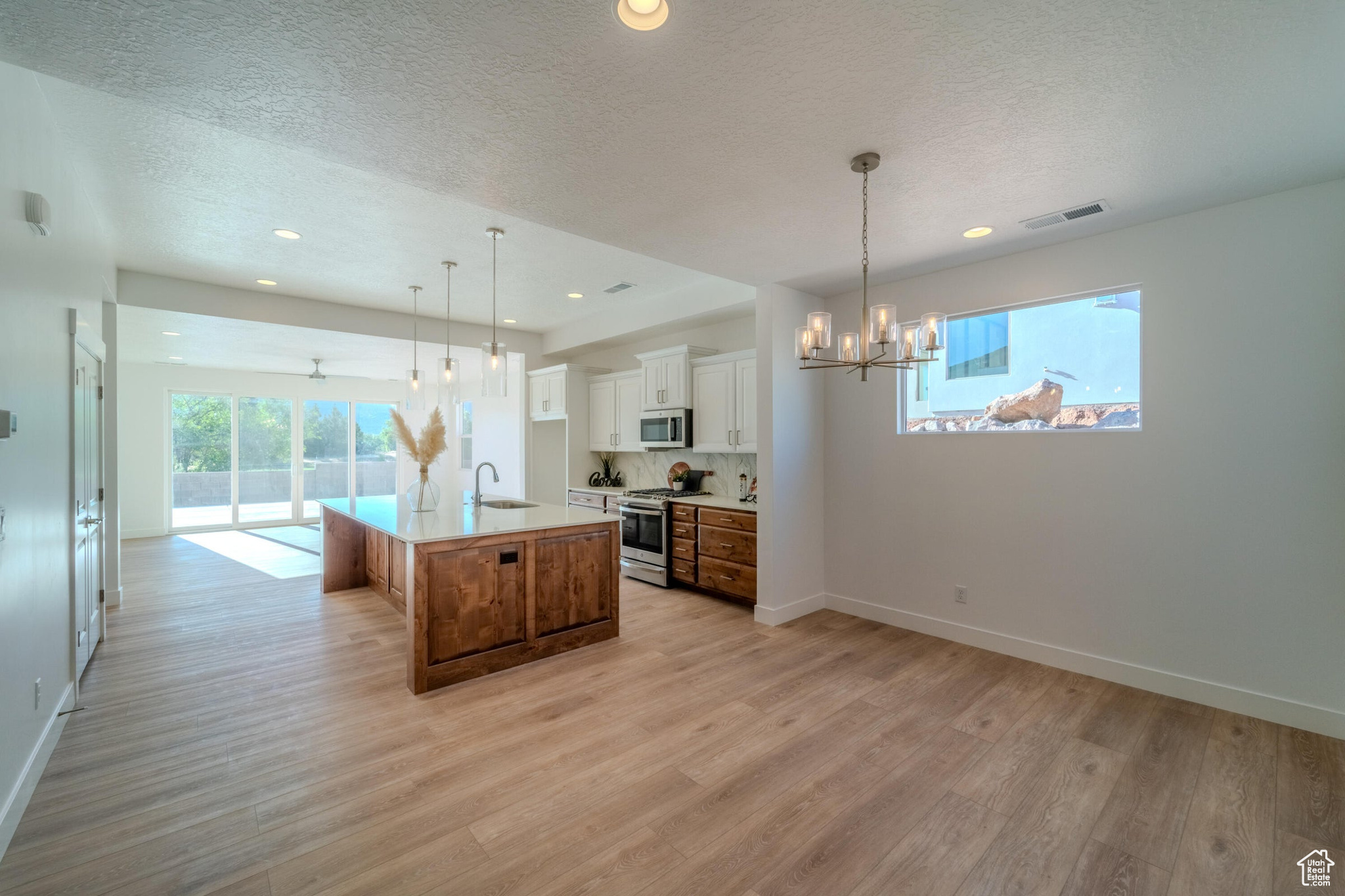 Kitchen with appliances with stainless steel finishes, a kitchen island with sink, light hardwood / wood-style flooring, and white cabinetry