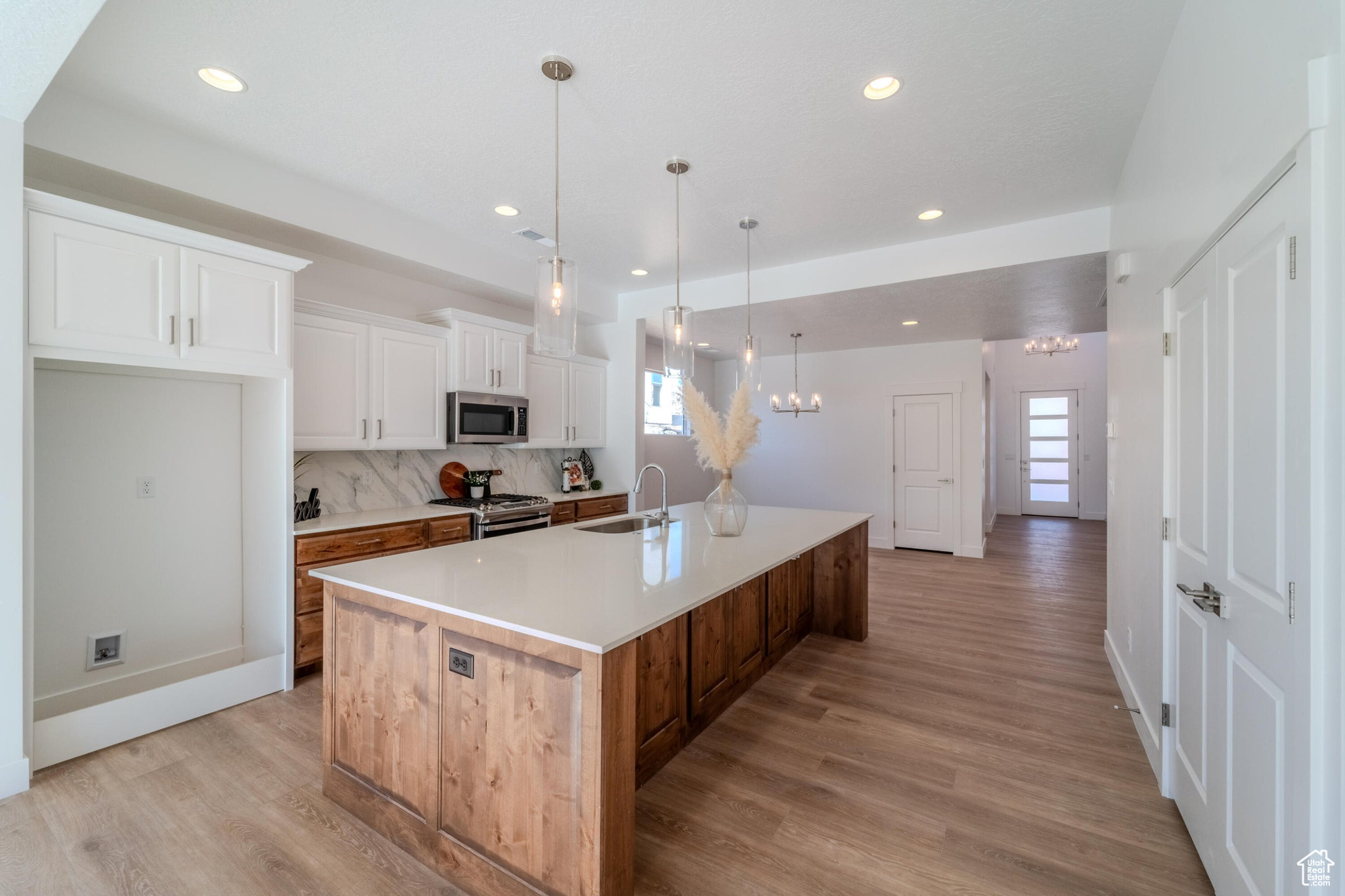 Kitchen with light hardwood / wood-style flooring, white cabinets, backsplash, stainless steel appliances, and a large island with sink