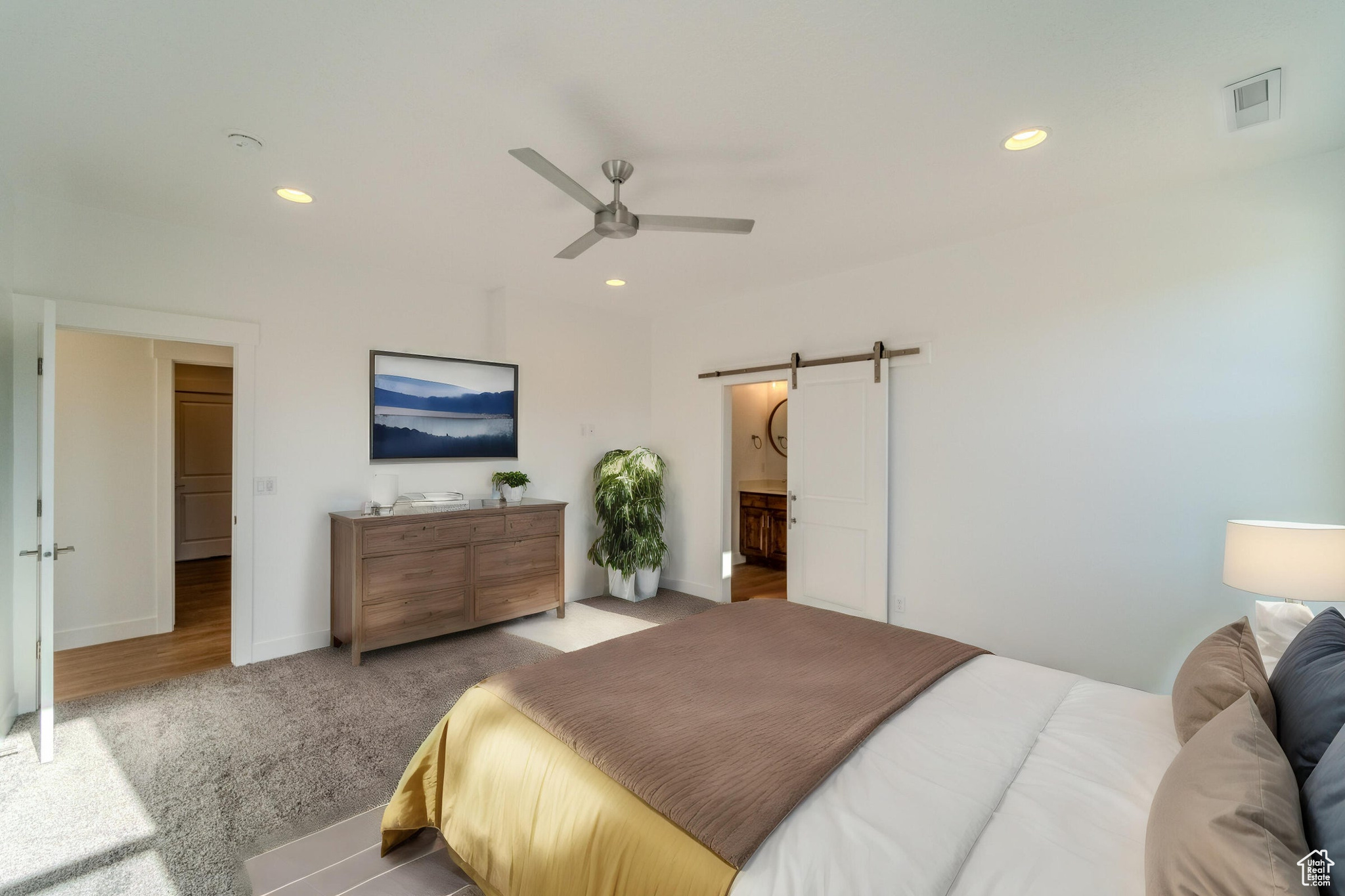 Carpeted bedroom featuring ensuite bath, ceiling fan, and a barn door