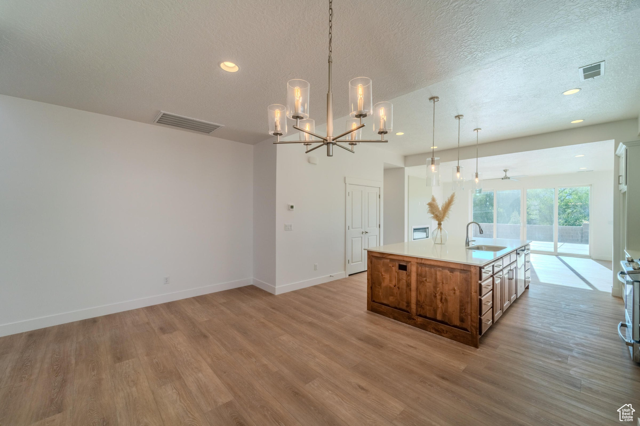 Kitchen featuring a textured ceiling, an island with sink, hardwood / wood-style flooring, decorative light fixtures, and sink