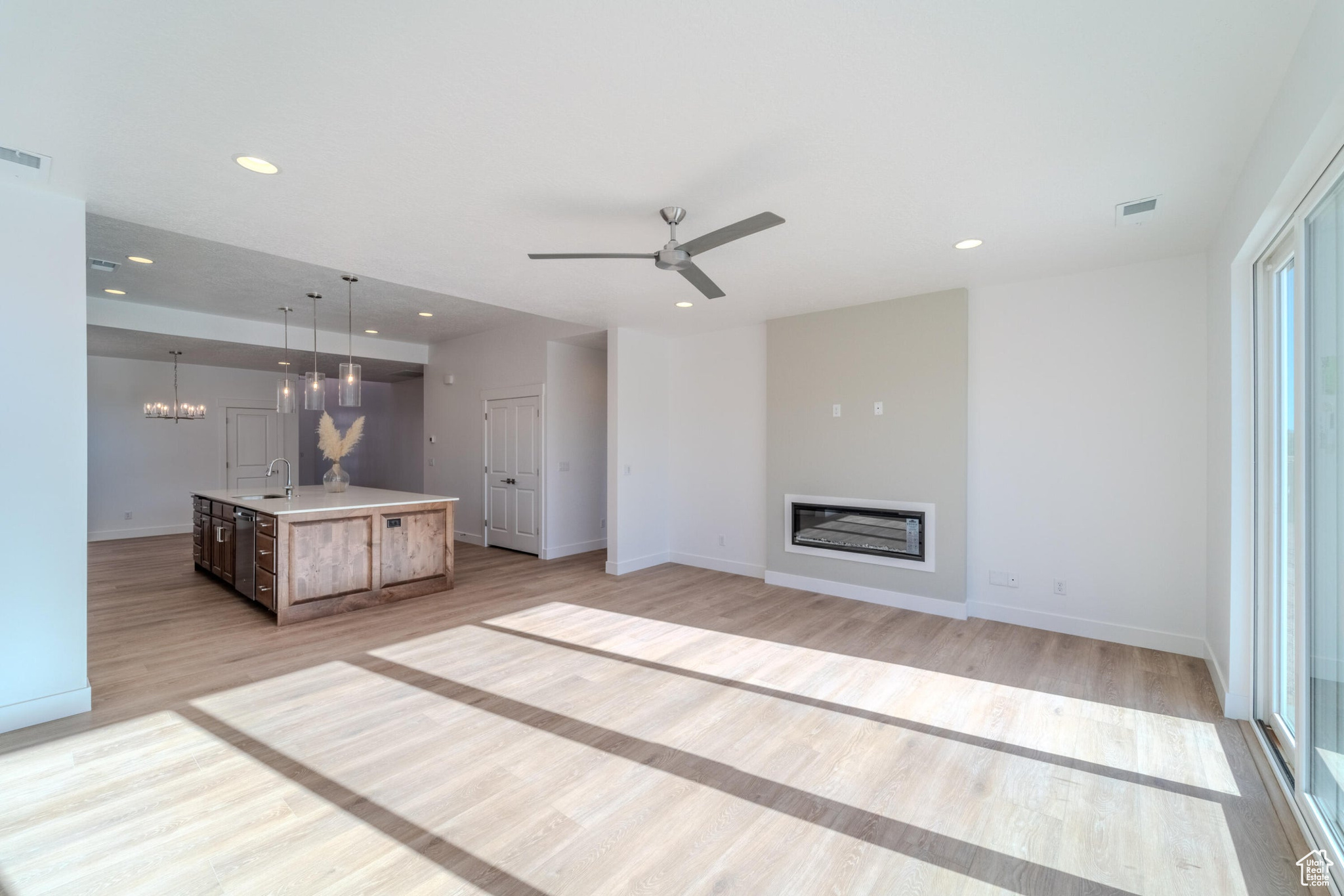 Unfurnished living room featuring sink, ceiling fan with notable chandelier, and light hardwood / wood-style flooring