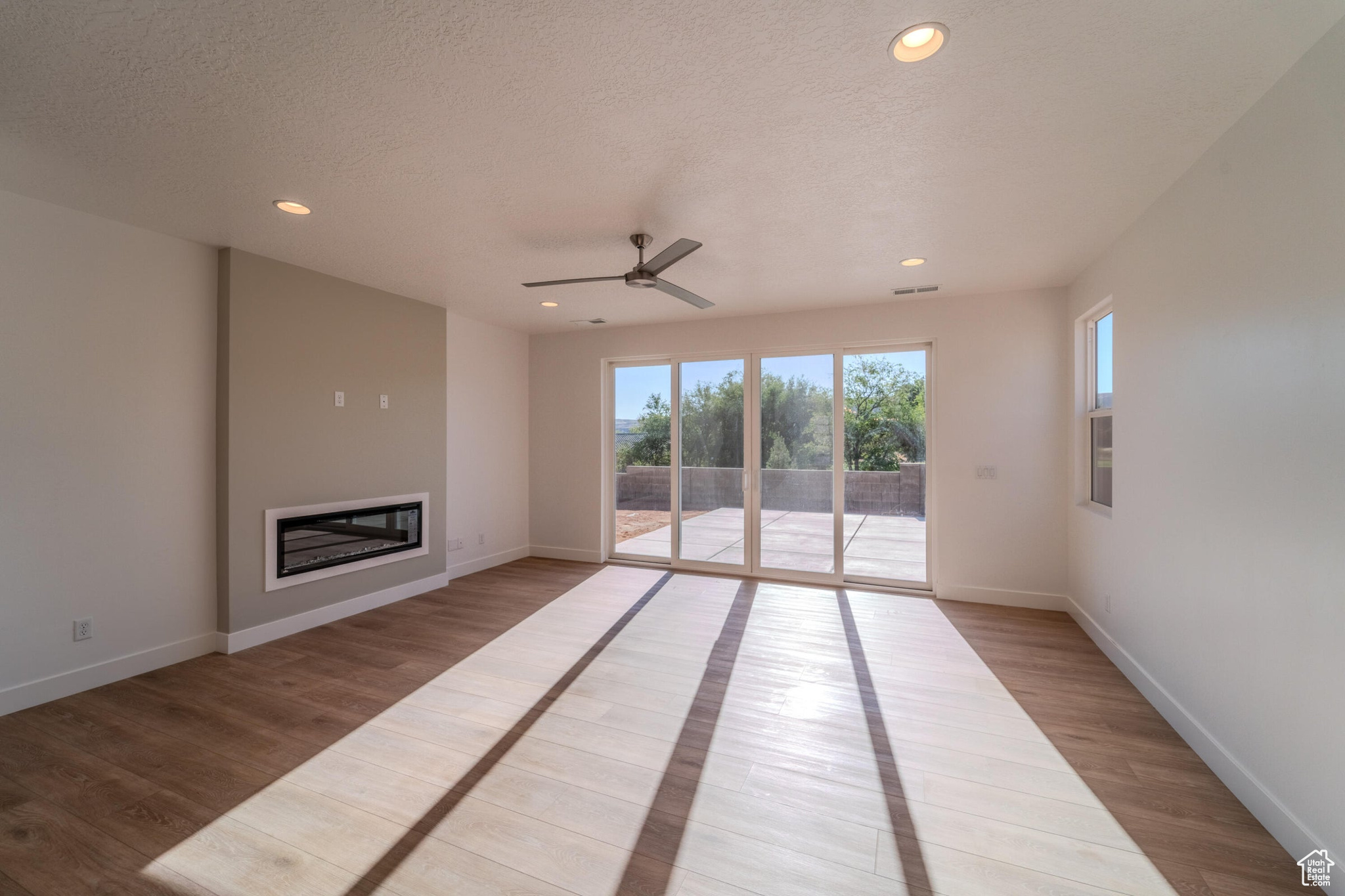 Unfurnished living room with light hardwood / wood-style flooring, a textured ceiling, and ceiling fan