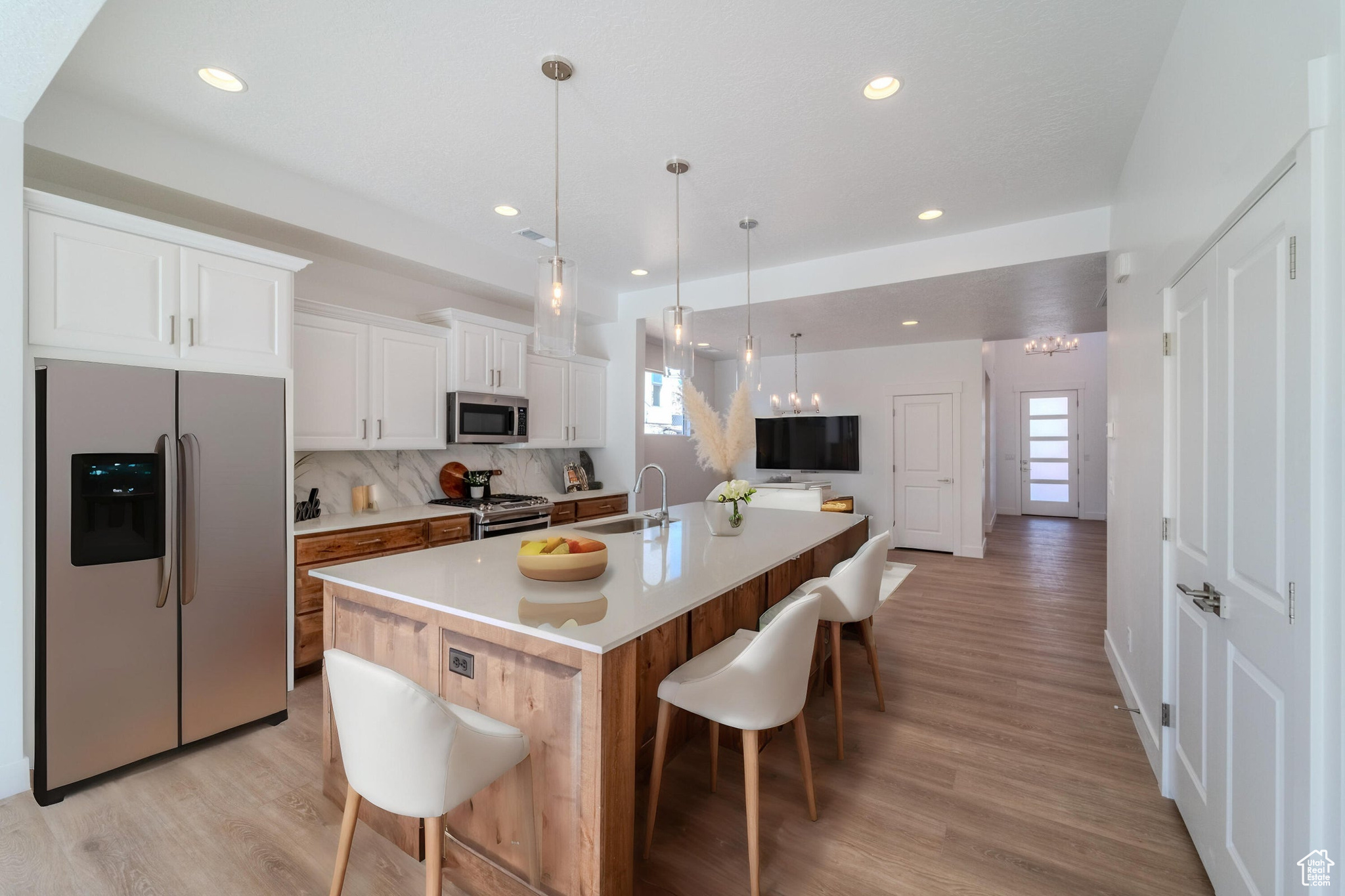 Kitchen with light hardwood / wood-style flooring, white cabinets, stainless steel appliances, backsplash, and an island with sink