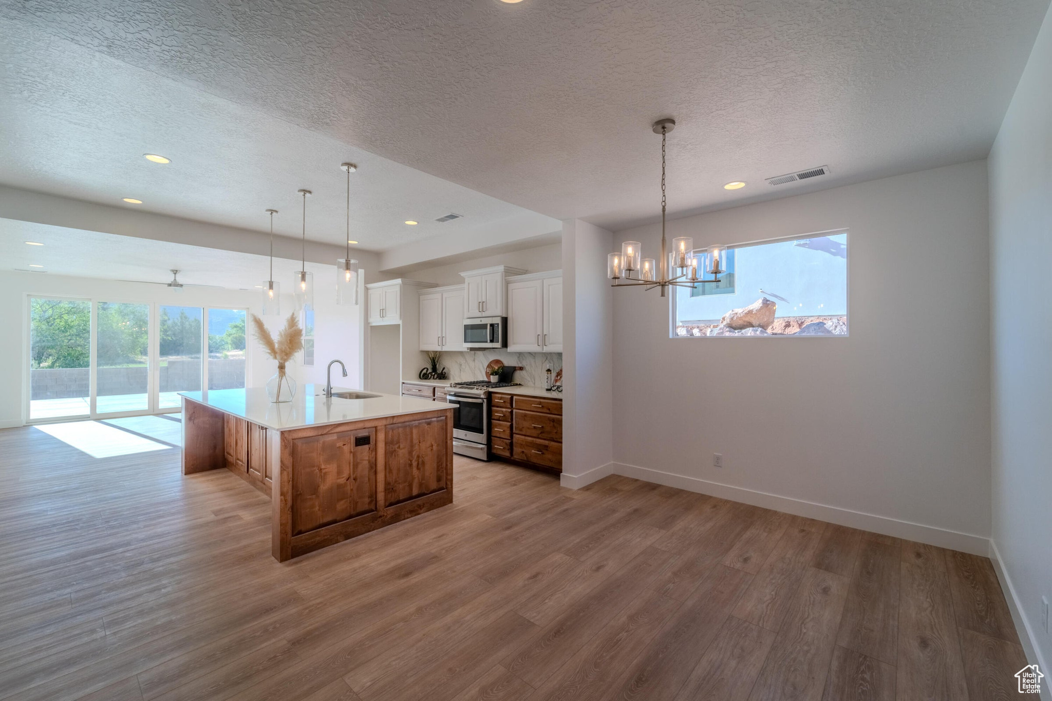 Kitchen with white cabinetry, light wood-type flooring, a center island with sink, range with gas stovetop, and sink