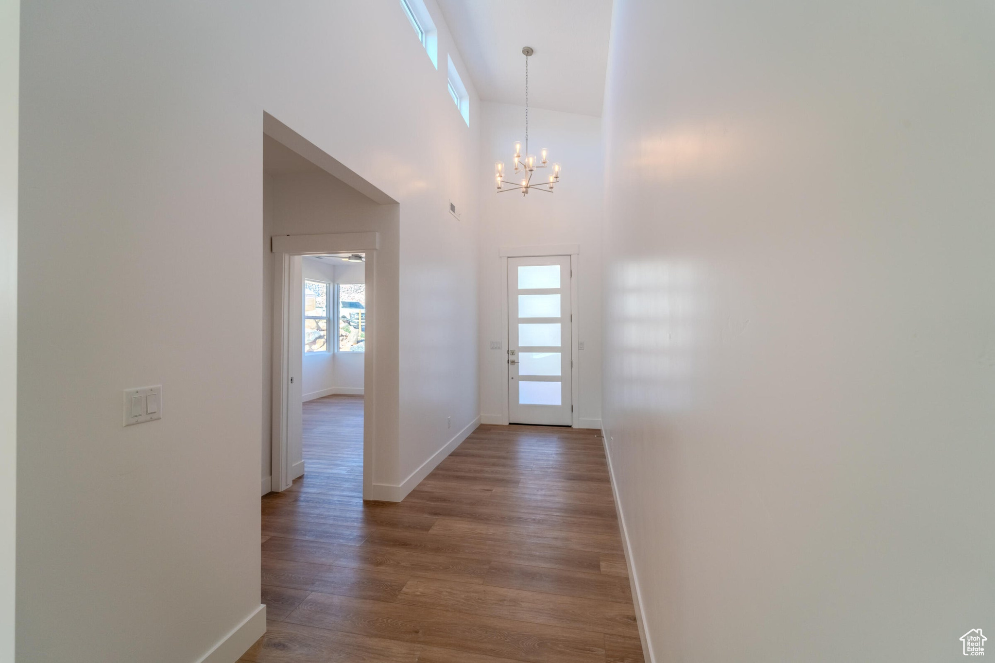 Hallway with high vaulted ceiling, hardwood / wood-style floors, and a chandelier