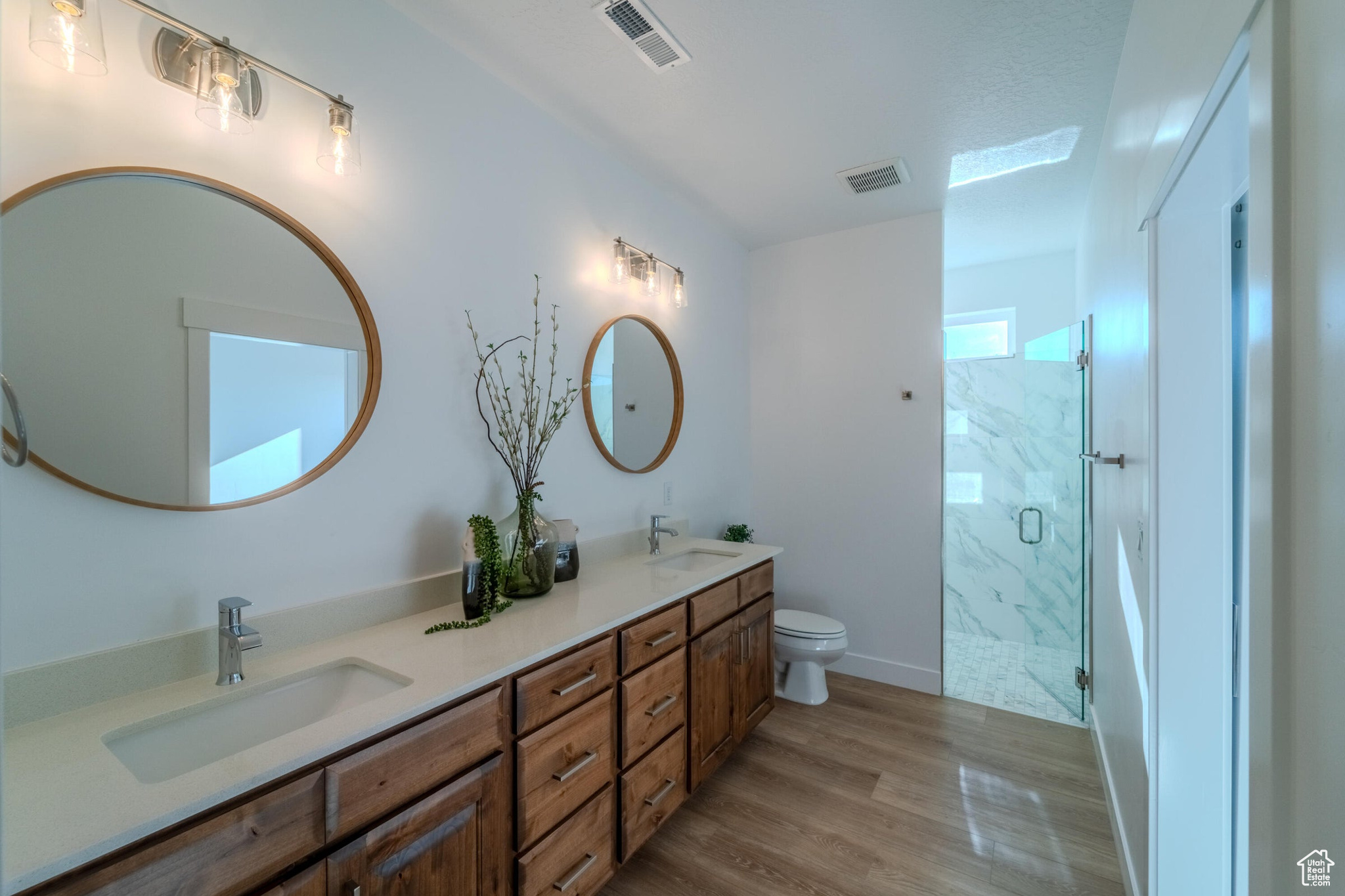 Bathroom featuring dual vanity, toilet, a shower with door, and hardwood / wood-style floors