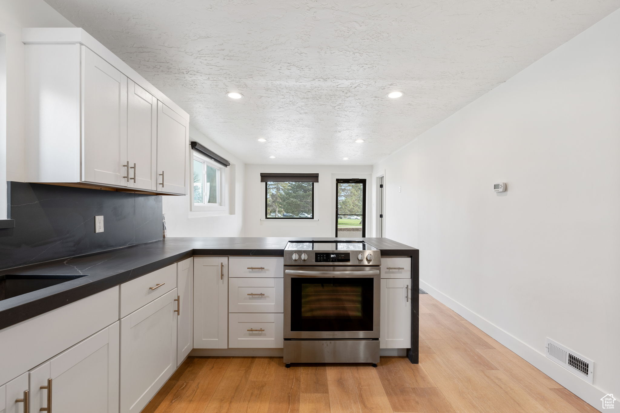 Kitchen featuring white cabinets, backsplash, light hardwood / wood-style floors, and electric stove