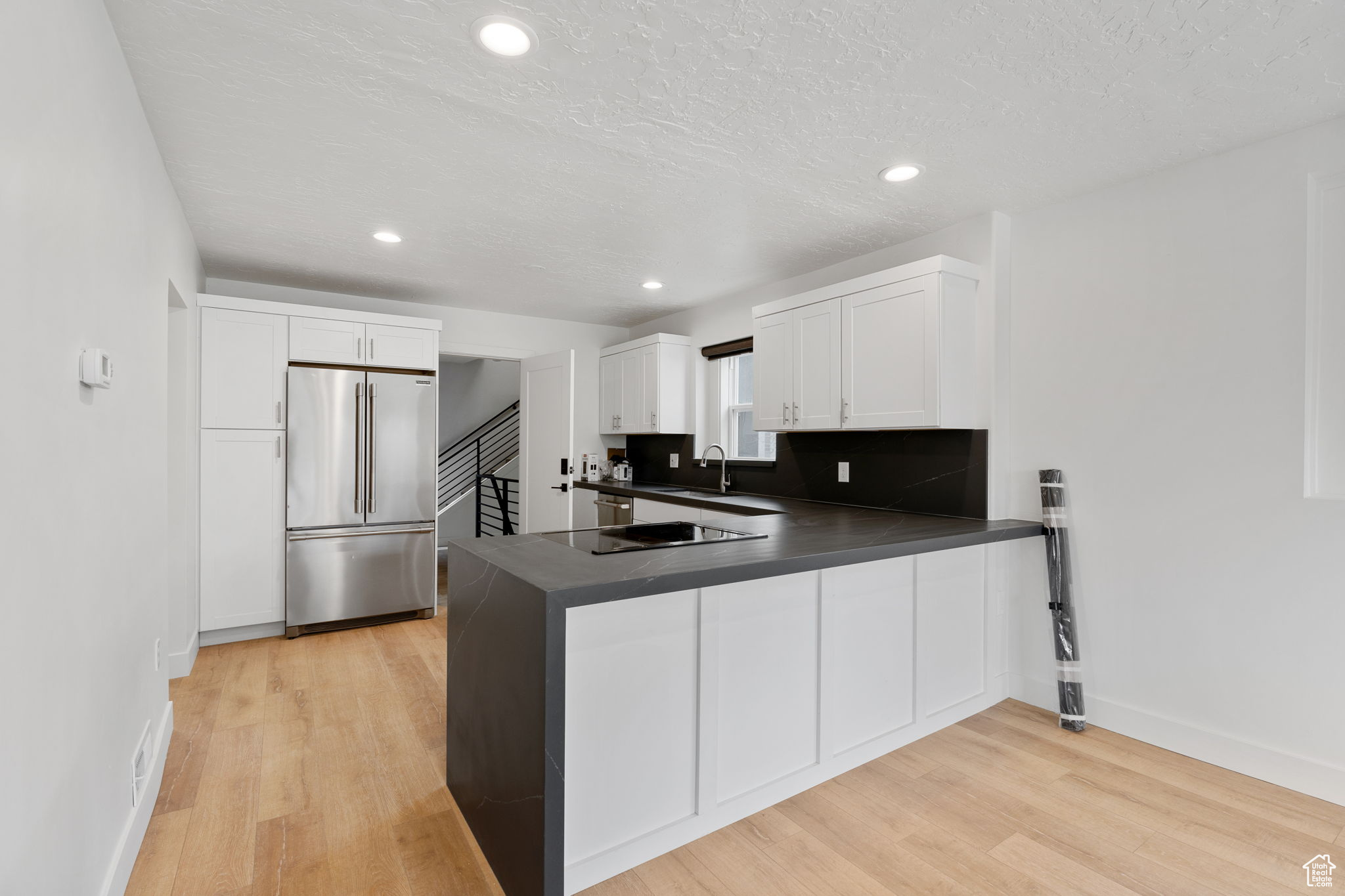 Kitchen with built in refrigerator, light hardwood / wood-style flooring, white cabinets, and kitchen peninsula