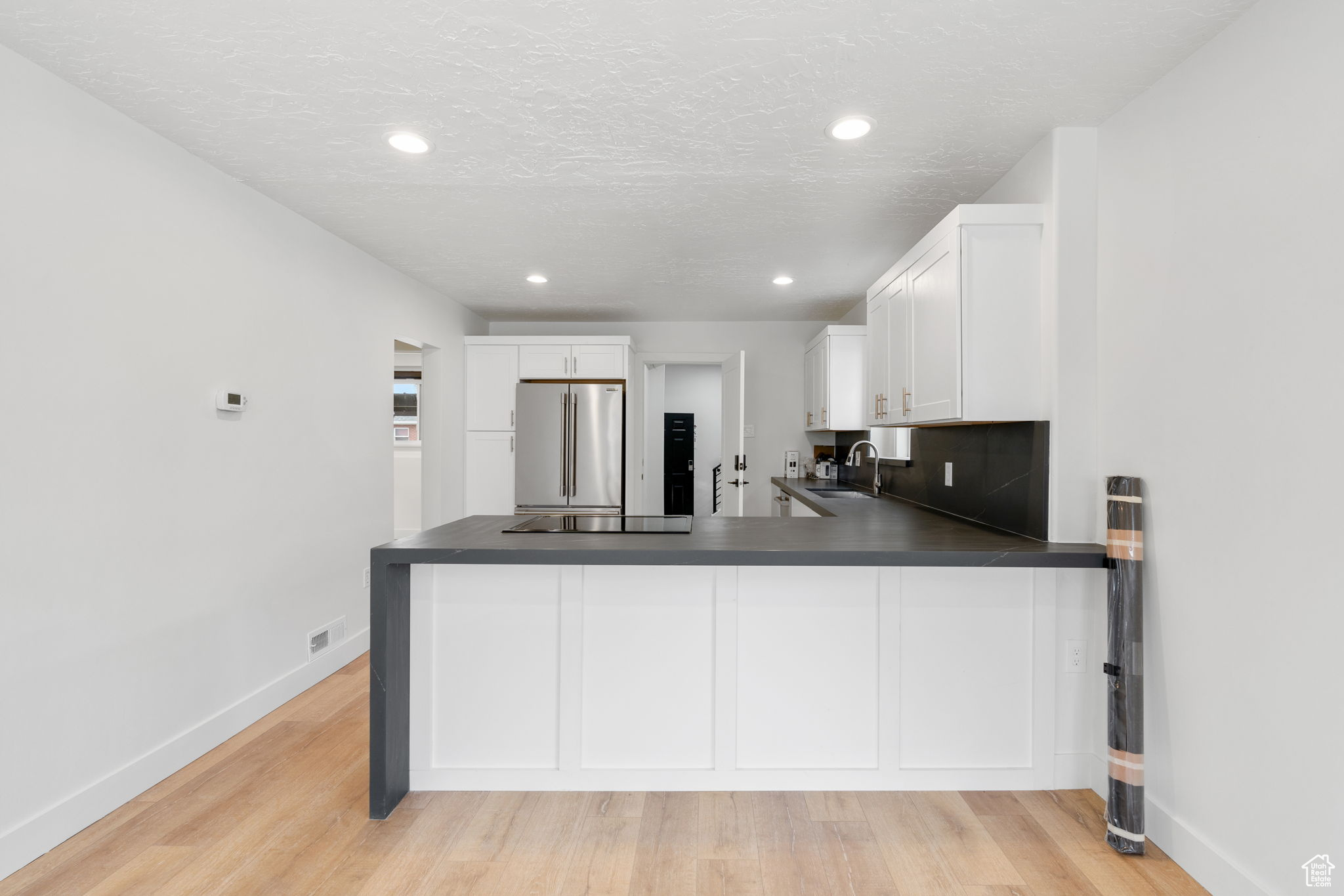 Kitchen with white cabinets, backsplash, high end fridge, and light wood-type flooring
