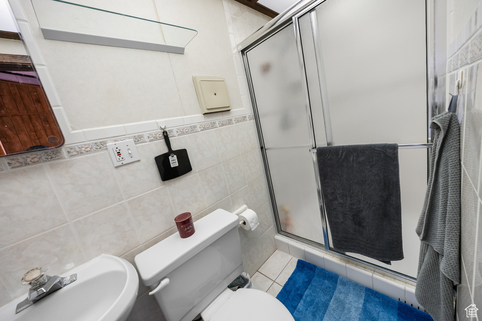Bathroom featuring tile floors, tile walls, a shower with shower door, sink, and toilet