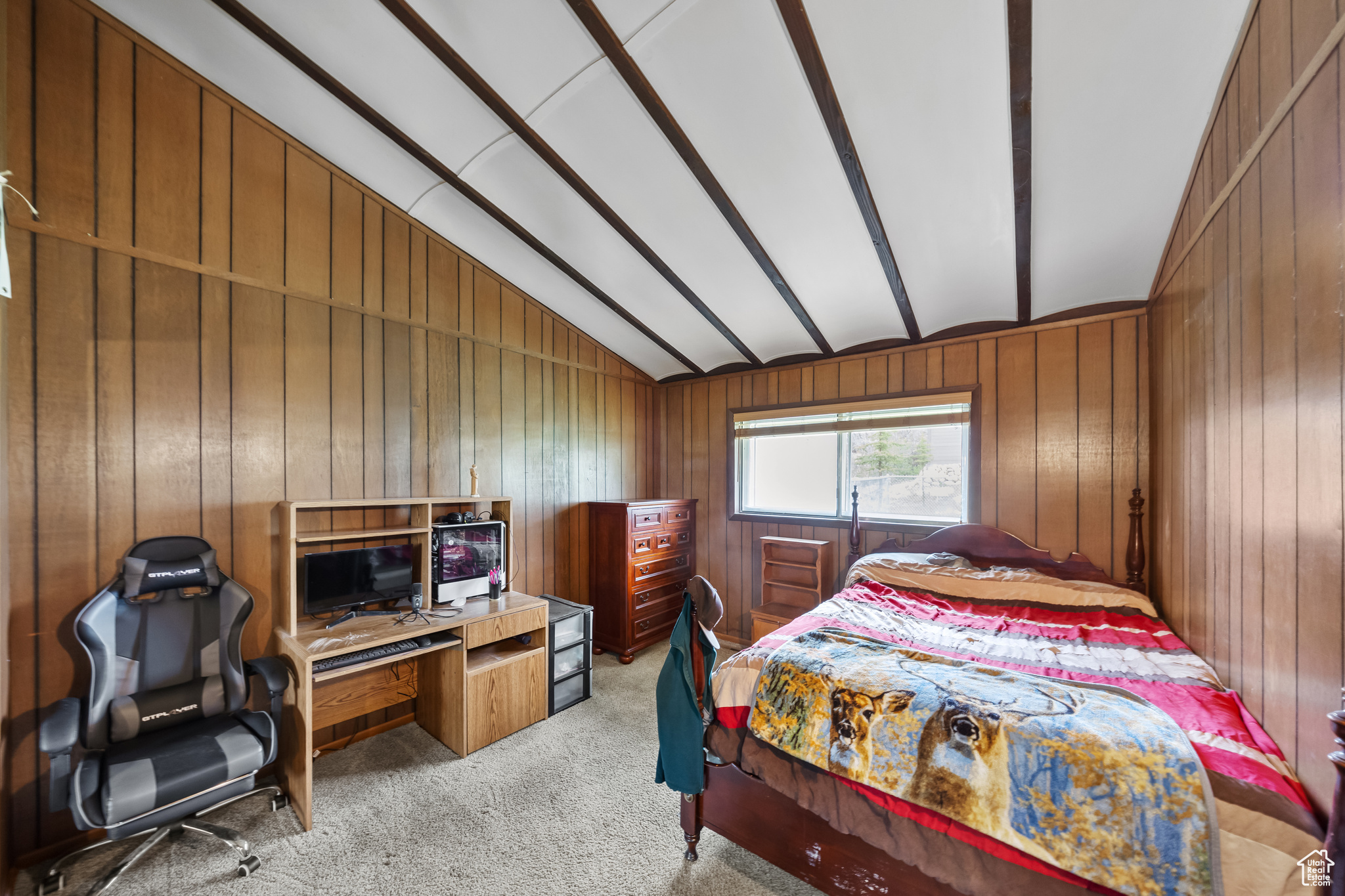 Carpeted bedroom with wood walls and vaulted ceiling with beams