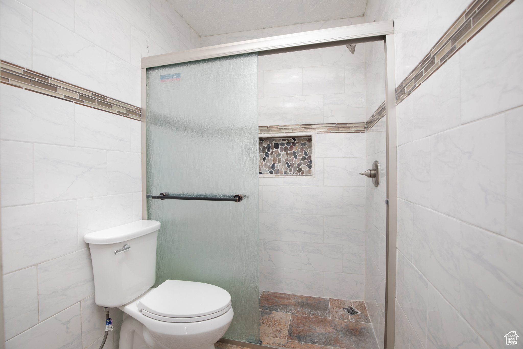 Bathroom featuring a shower with door, toilet, and tile walls