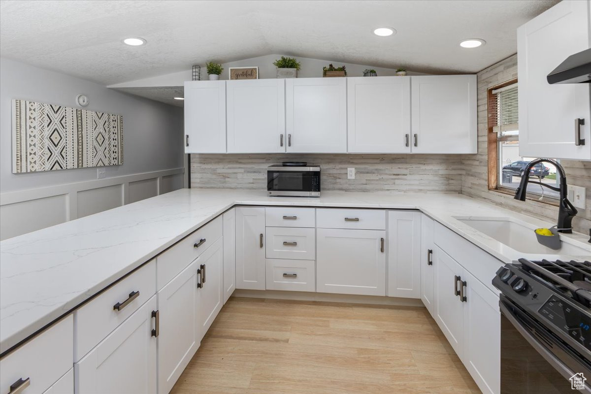 Kitchen with white cabinetry, vaulted ceiling, tasteful backsplash, light stone counters, and light wood-type flooring