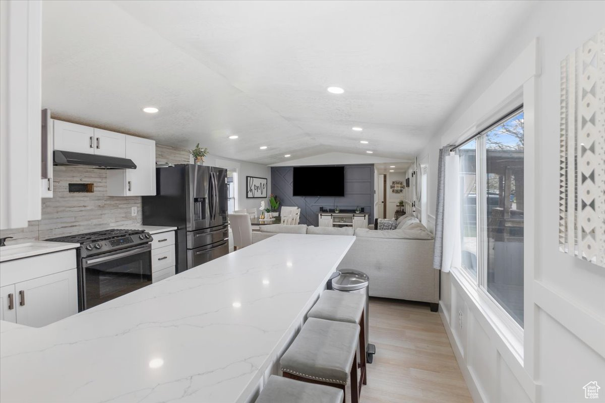 Kitchen with white cabinets, gas stove, vaulted ceiling, and stainless steel fridge