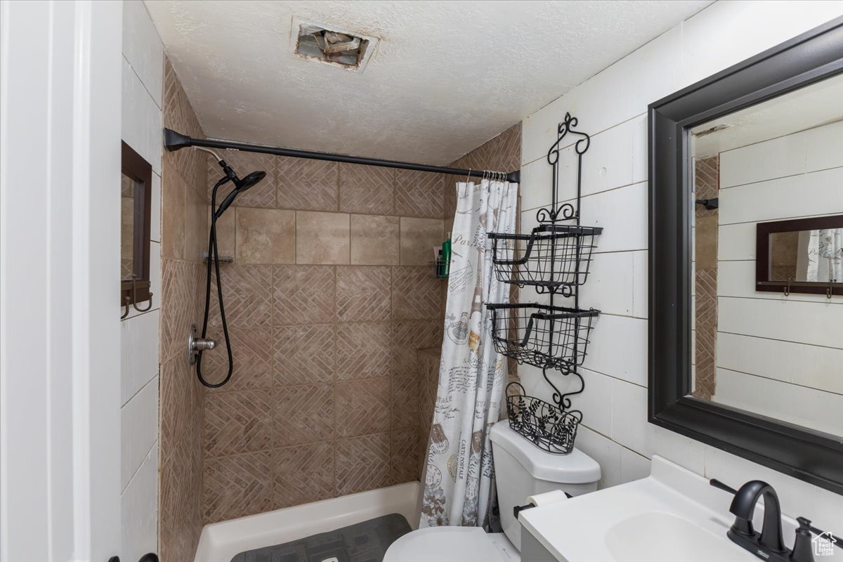 Full bathroom with shower / bath combination with curtain, tile walls, vanity, toilet, and a textured ceiling