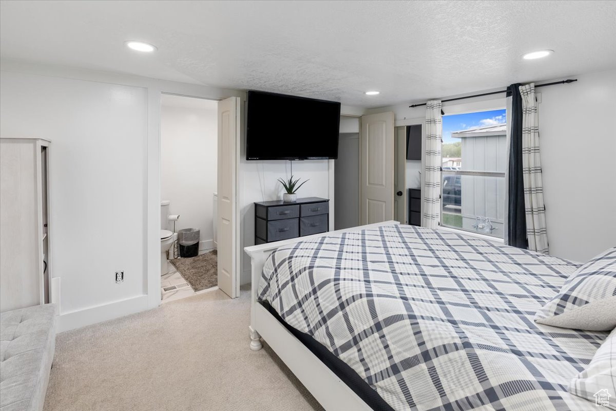 Bedroom featuring light colored carpet, ensuite bathroom, and a textured ceiling