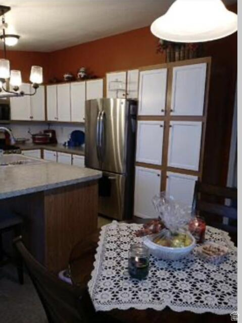 Kitchen featuring decorative light fixtures, stove, stainless steel refrigerator, white cabinetry, and a chandelier