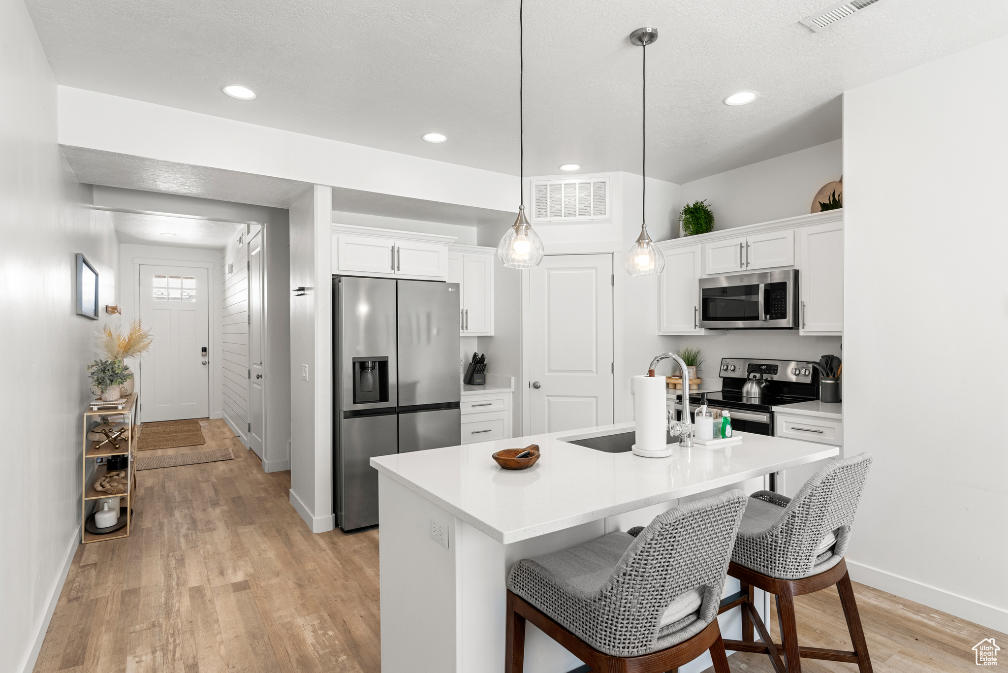 Kitchen featuring pendant lighting, light hardwood / wood-style floors, white cabinetry, stainless steel appliances, and a kitchen island with sink