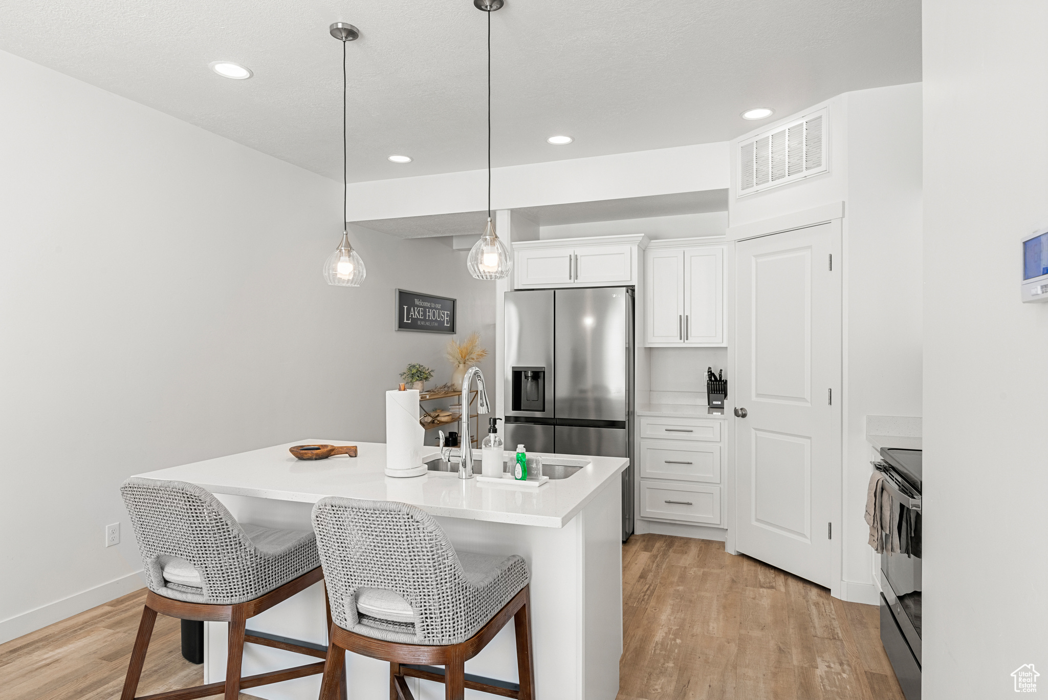 Kitchen with pendant lighting, stainless steel appliances, light hardwood / wood-style floors, and white cabinetry