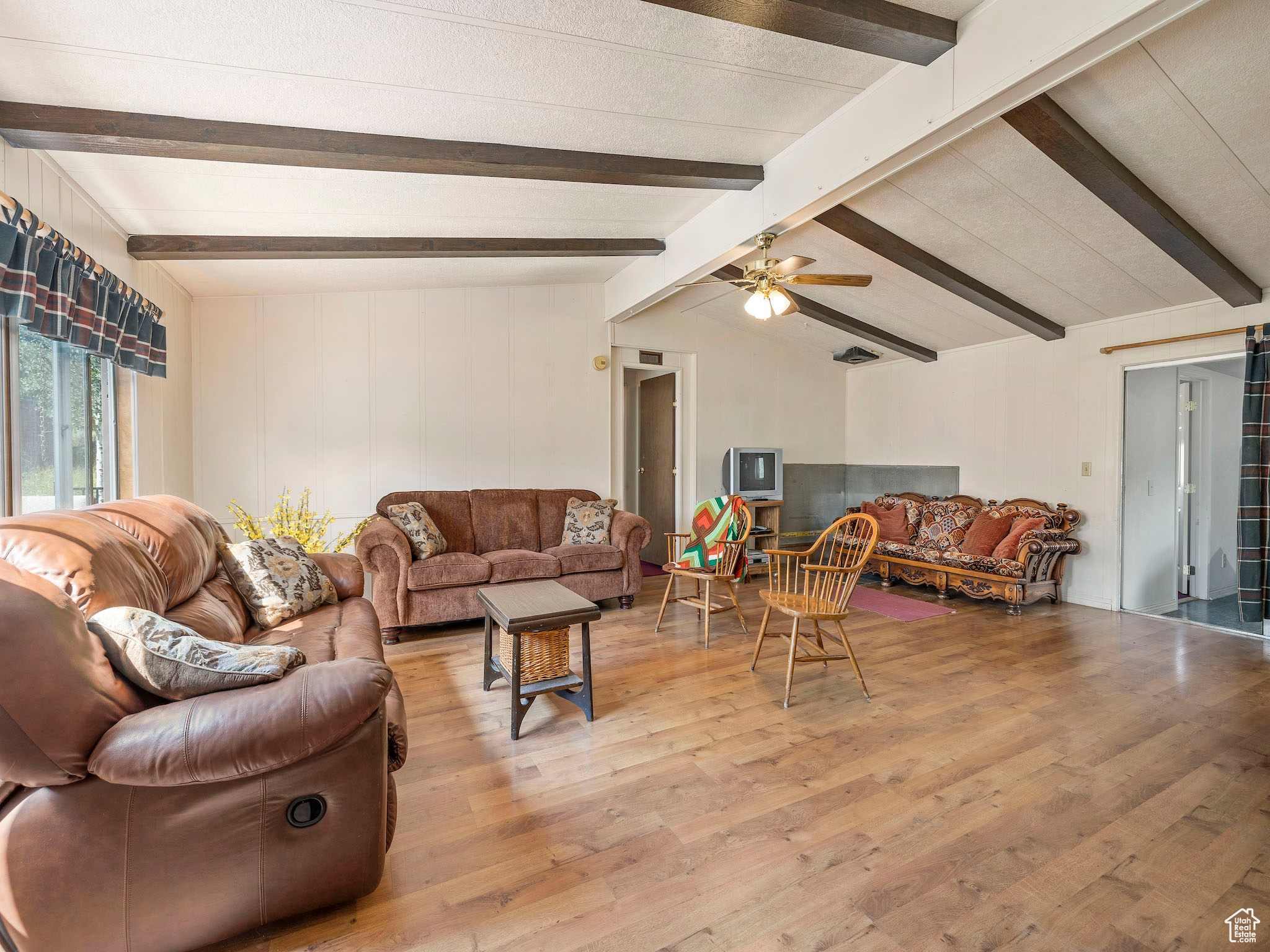 Living room featuring light wood-type flooring, ceiling fan, and vaulted ceiling with beams