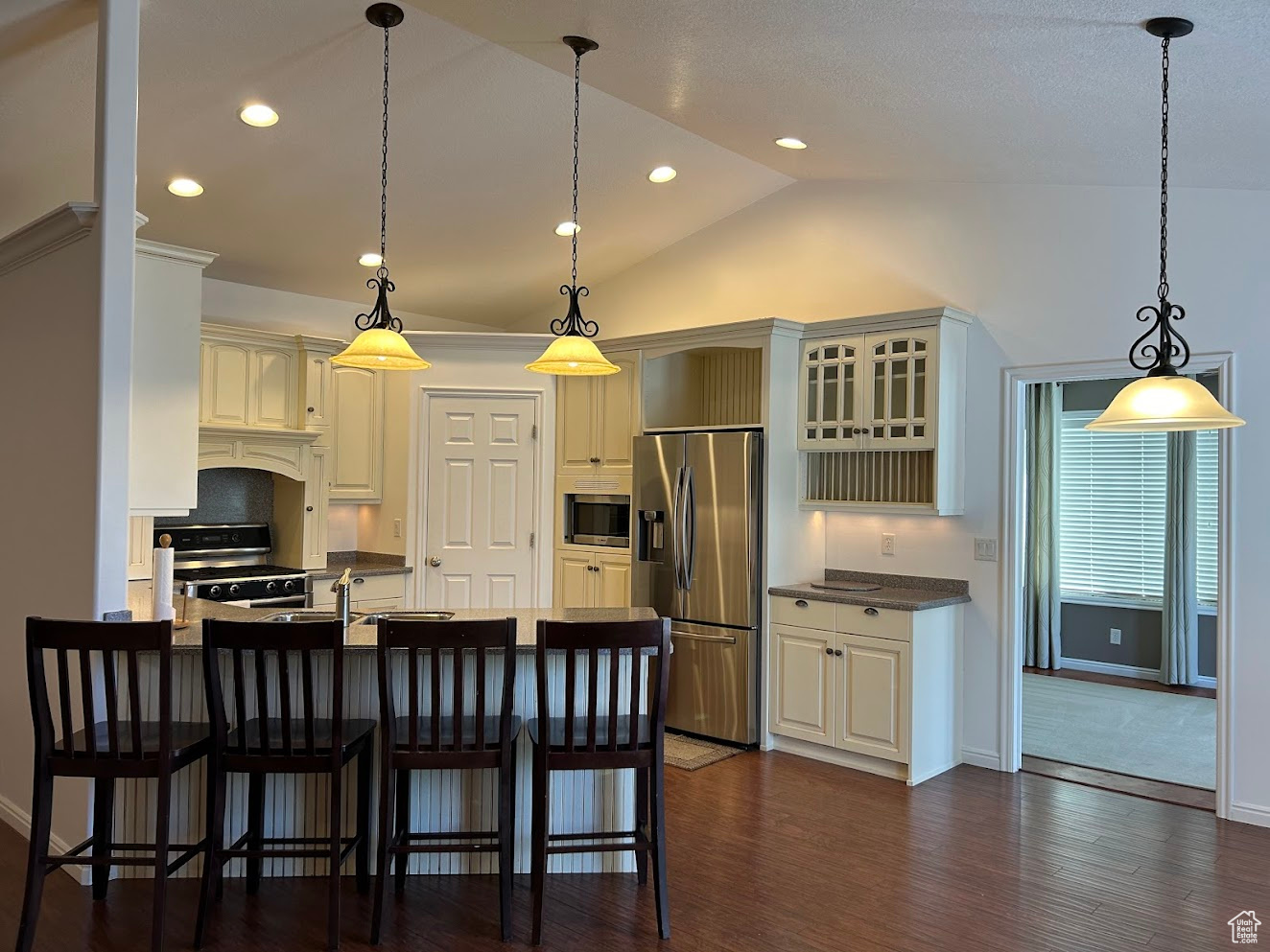 Kitchen with stainless steel appliances, pendant lighting, lofted ceiling, a kitchen breakfast bar, and dark wood-type flooring