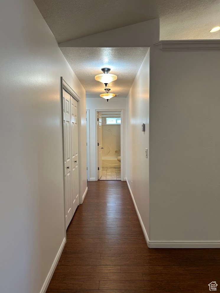 Hall featuring vaulted ceiling, dark hardwood / wood-style flooring, and a textured ceiling