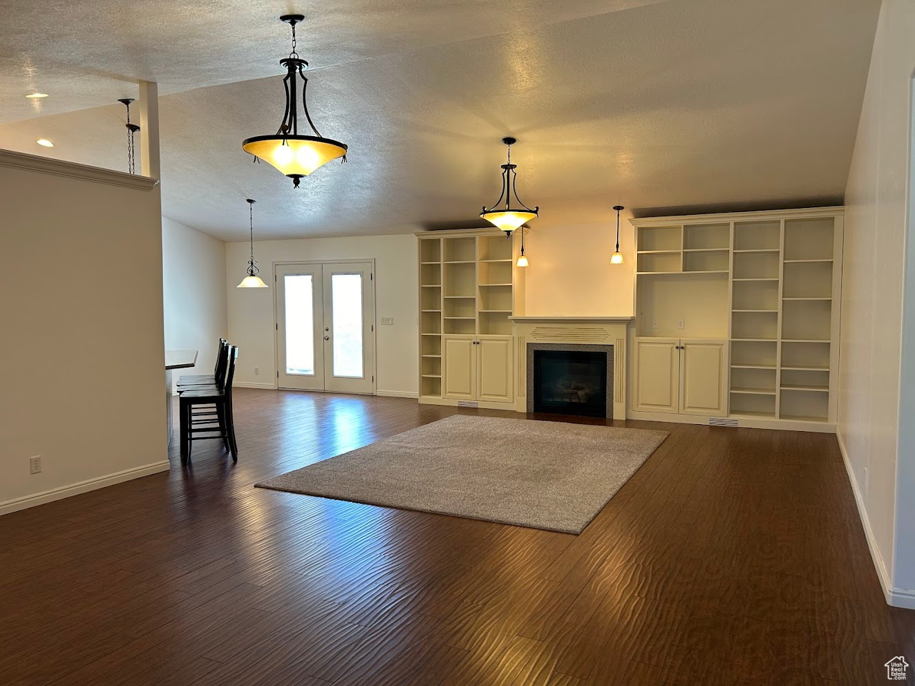 Unfurnished living room with a textured ceiling, dark hardwood / wood-style flooring, and french doors