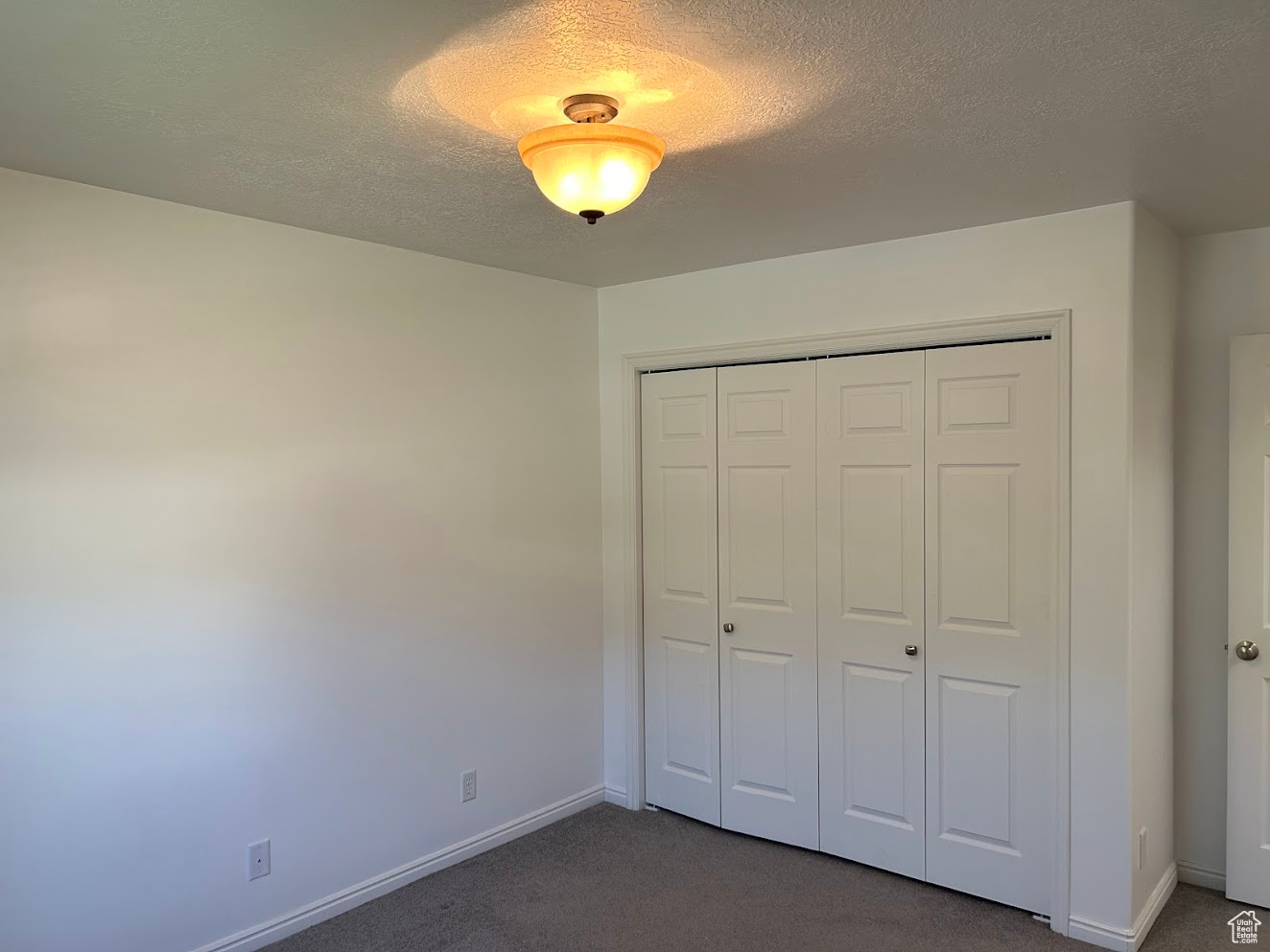 Unfurnished bedroom with dark carpet, a textured ceiling, and a closet