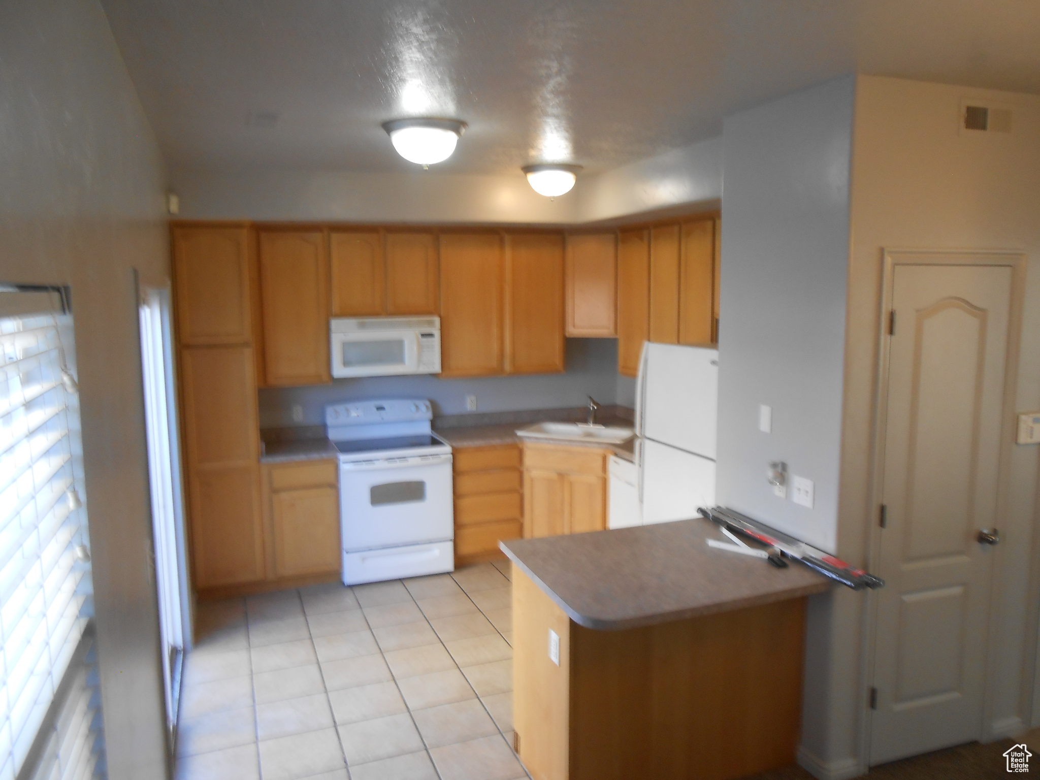 Kitchen with sink, white appliances, light tile flooring, and kitchen peninsula