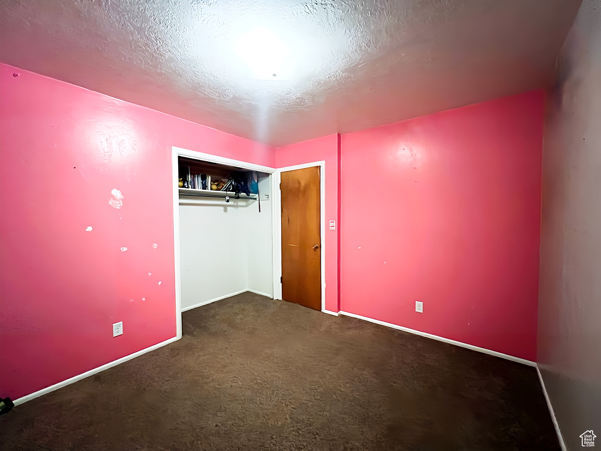 Unfurnished bedroom featuring a textured ceiling, dark carpet, and a closet