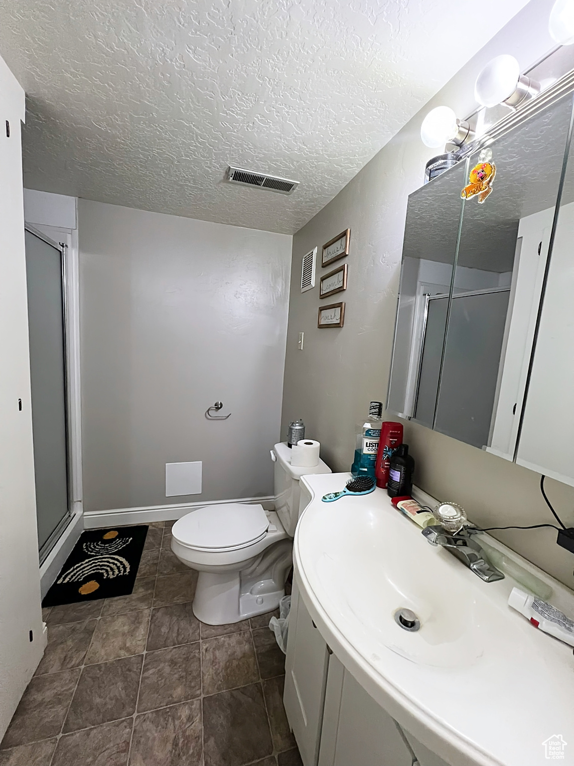 Bathroom with a textured ceiling, vanity, toilet, and walk in shower