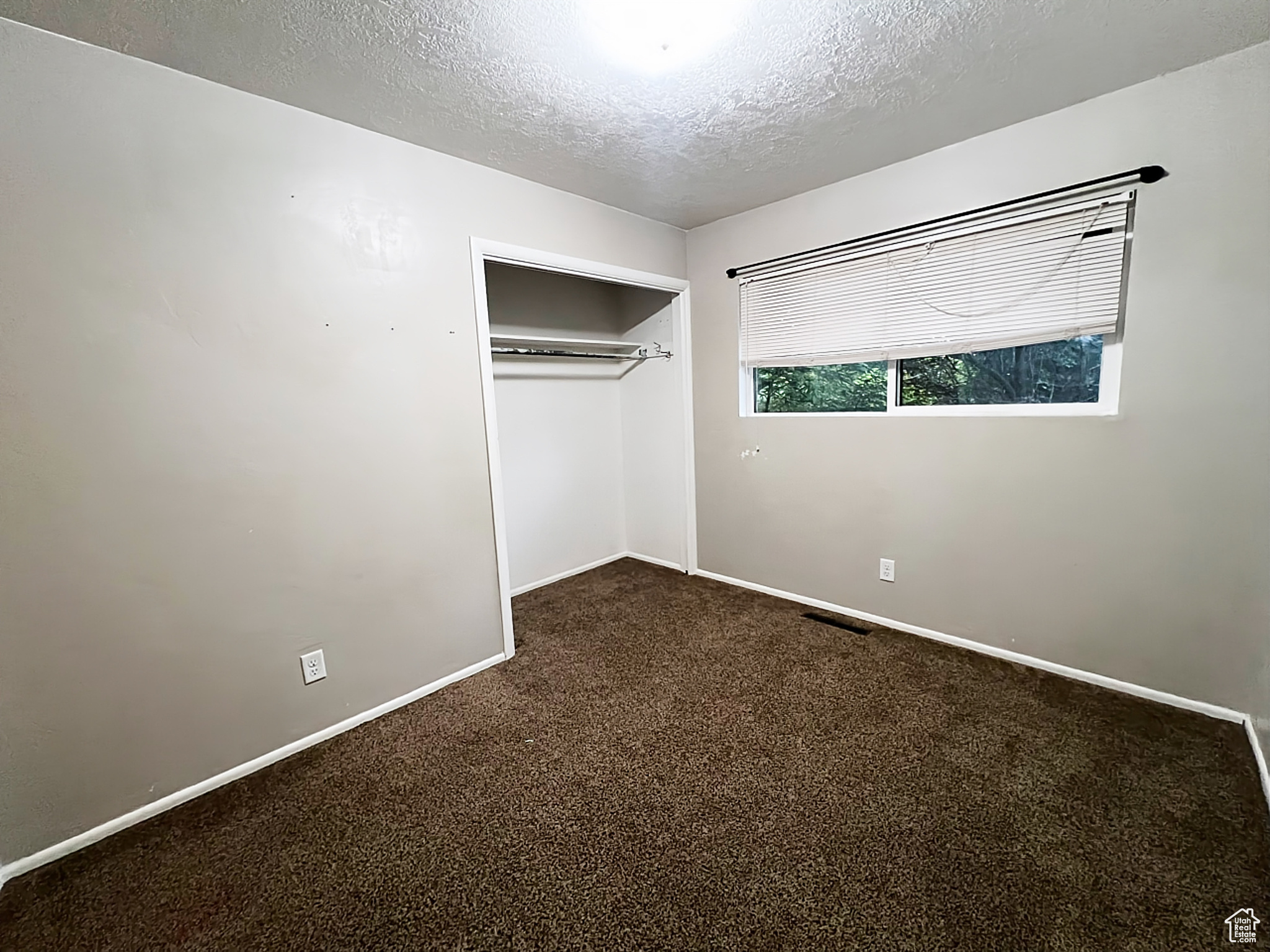 Unfurnished bedroom with a textured ceiling, carpet flooring, and a closet