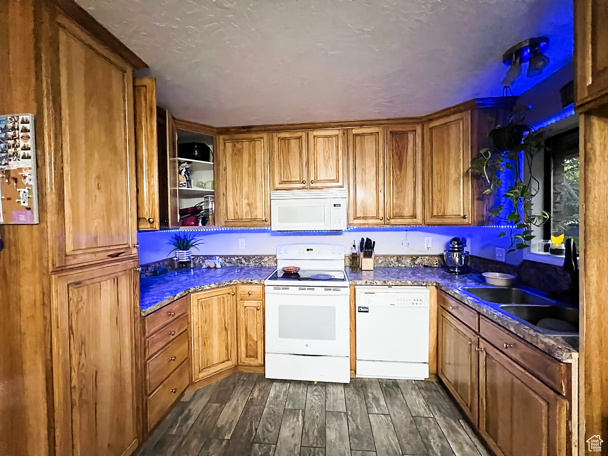 Kitchen with a textured ceiling, dark wood-type flooring, and white appliances